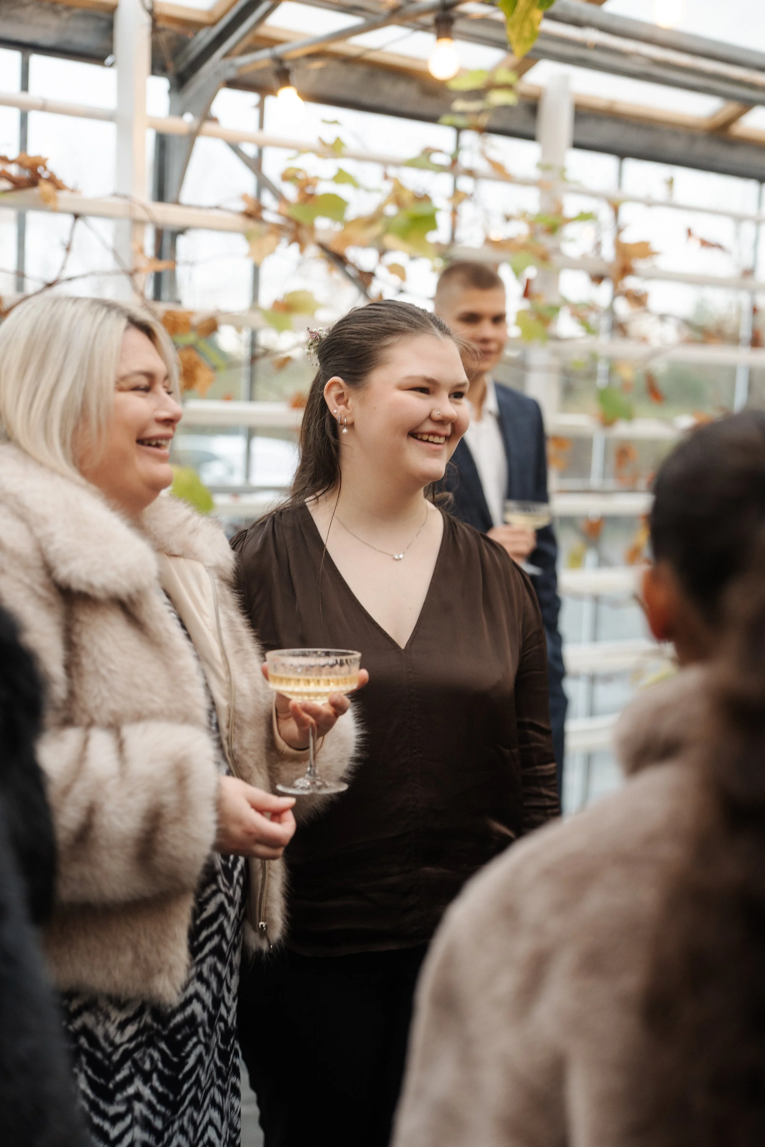 People enjoying a social gathering indoors, with a woman holding a champagne glass, smiling, and others engaging in conversation.