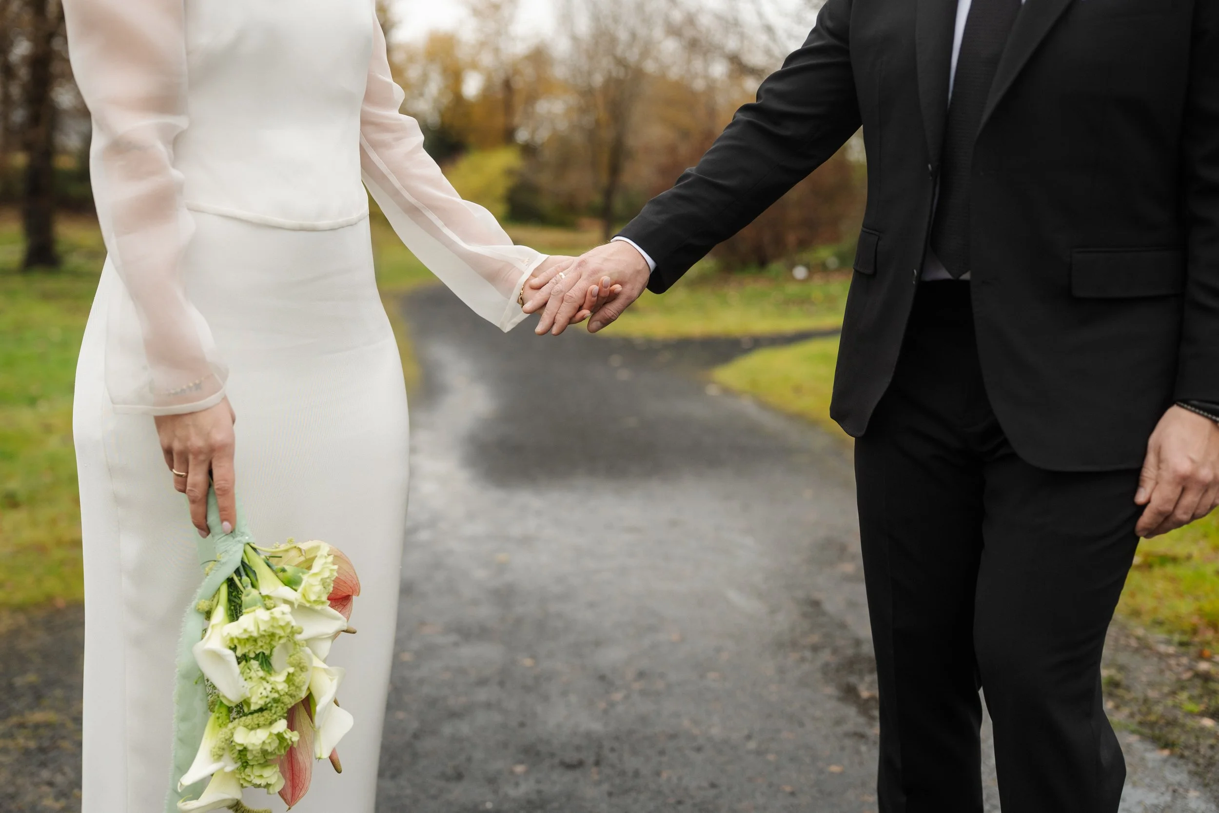A bride and groom holding hands outdoors on a rainy day, with the bride holding a bouquet of flowers.