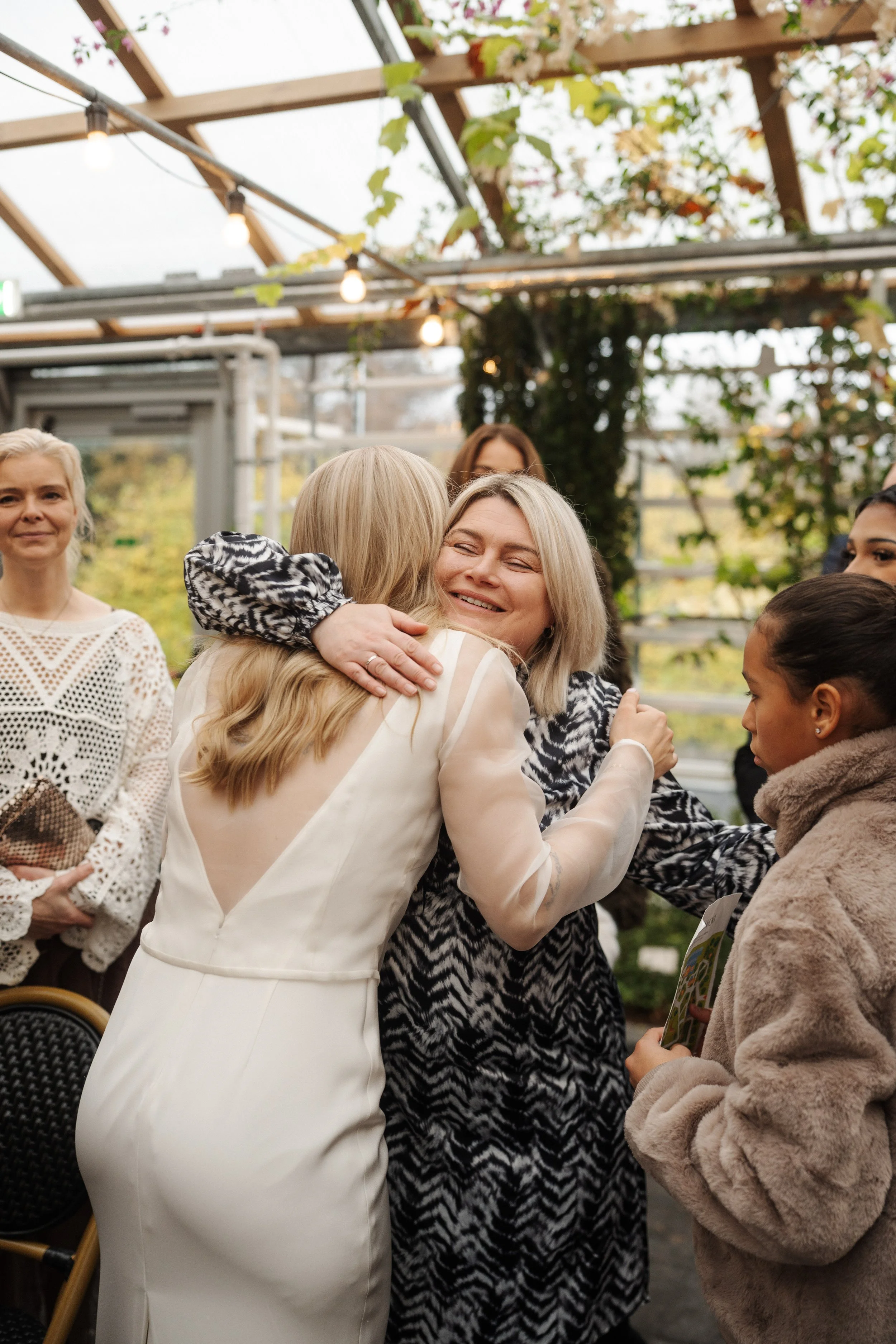 Women hugging each other at a gathering outdoors, with others smiling and watching in the background.