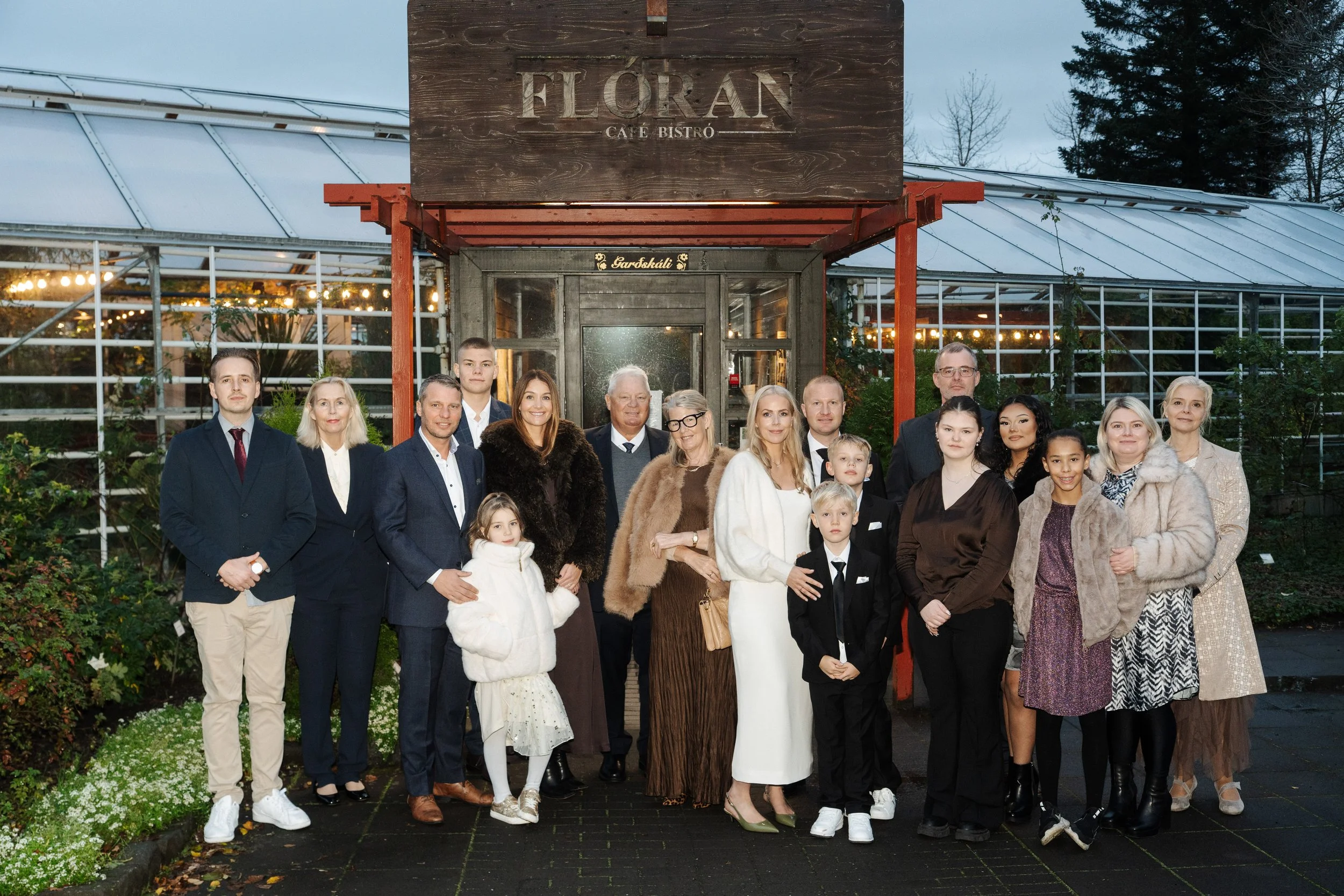 Group of people, including adults and children, standing outside a restaurant named Floran Café Bistró, posing for a photo in front of the entrance during dusk.