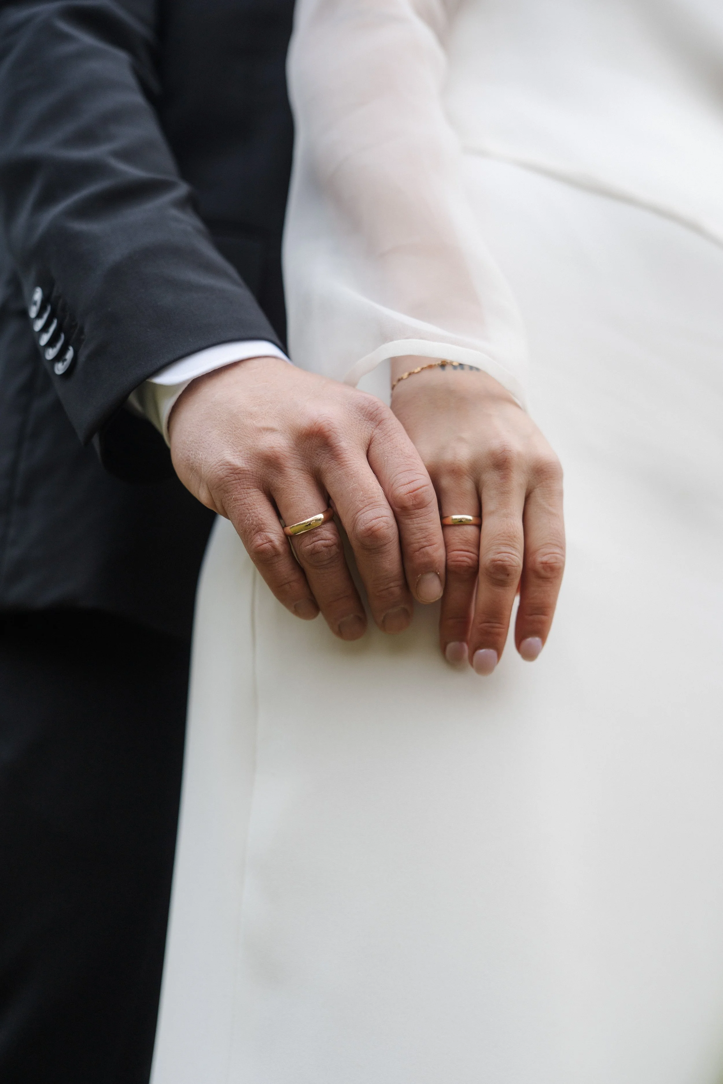 Close-up of a bride and groom's hands with wedding rings resting on a white surface.