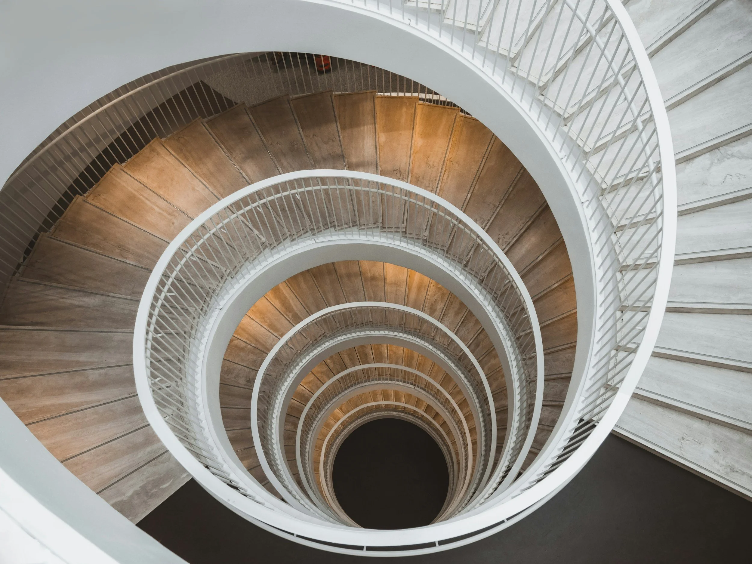 Looking down a spiral staircase with wooden steps and white railings.
