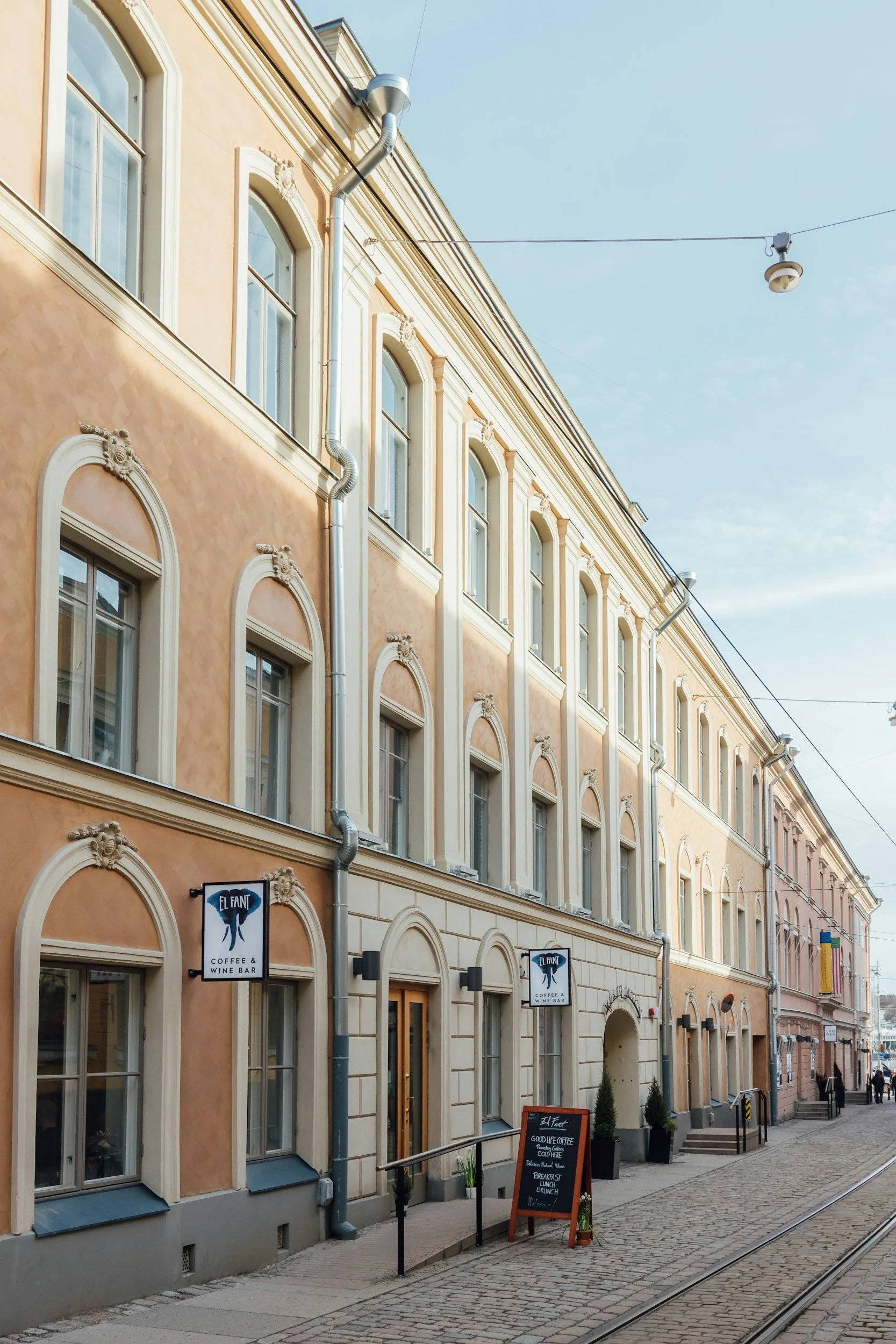 A pastel-colored building with multiple windows, signage for a coffee and wine bar, and a chalkboard menu placed on the sidewalk near the entrance.