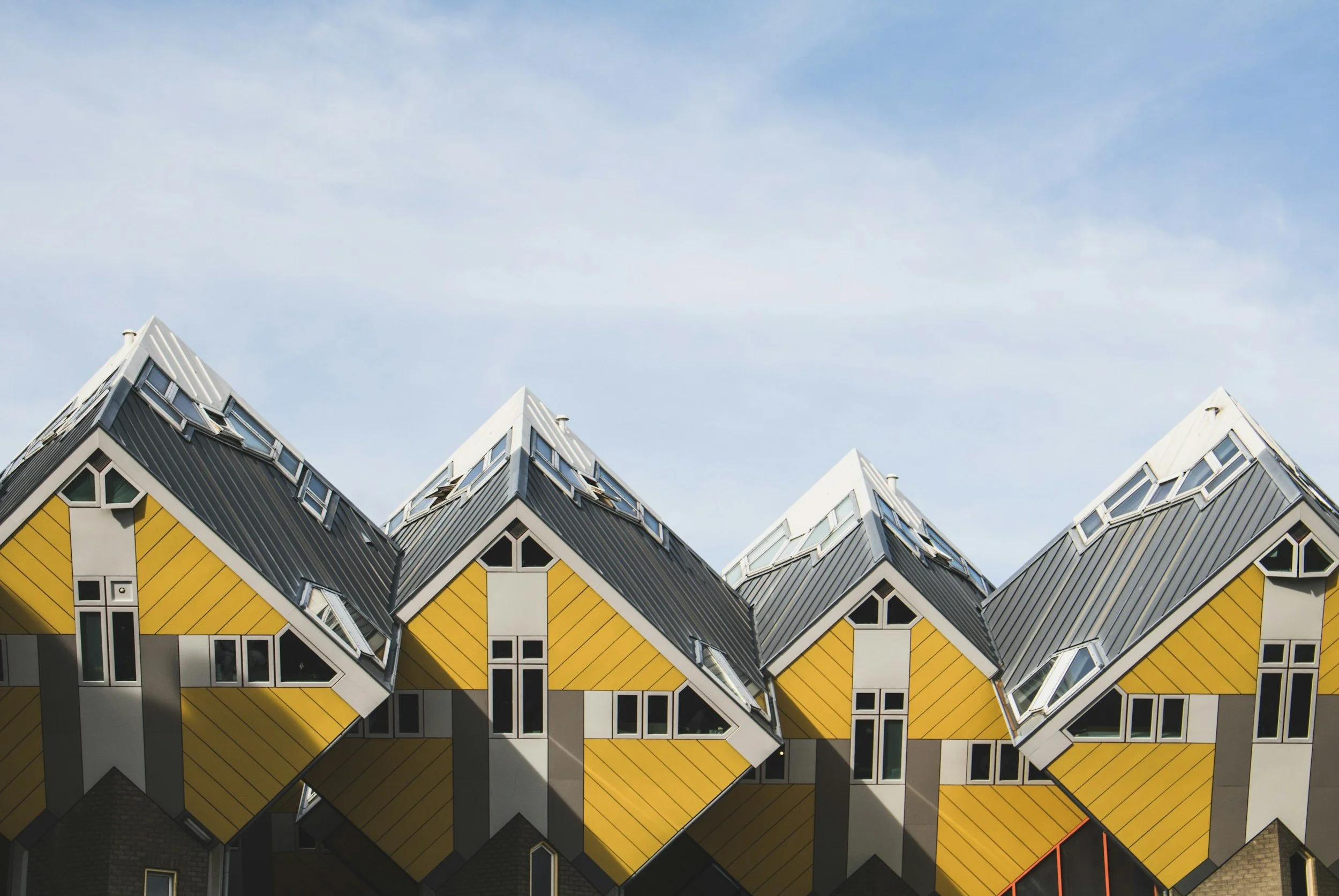 Unique tilted yellow houses with black roofs and multiple windows against a blue sky.