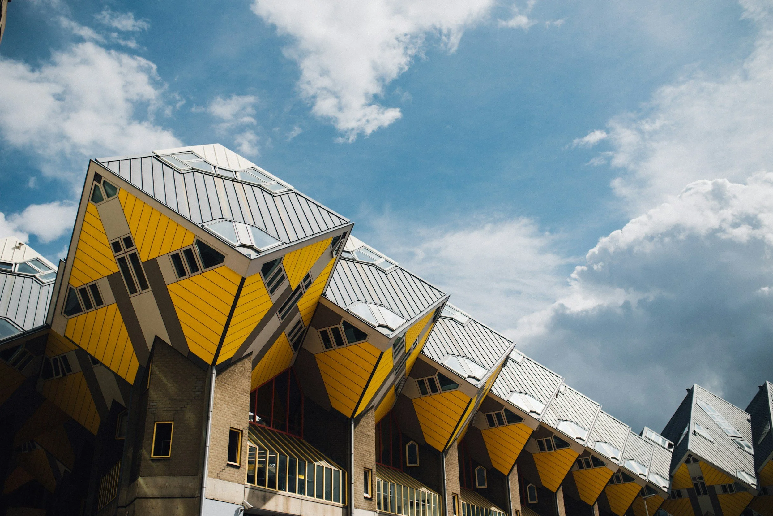Modern building with yellow cube-shaped structures supported by concrete pillars, under a partly cloudy sky.