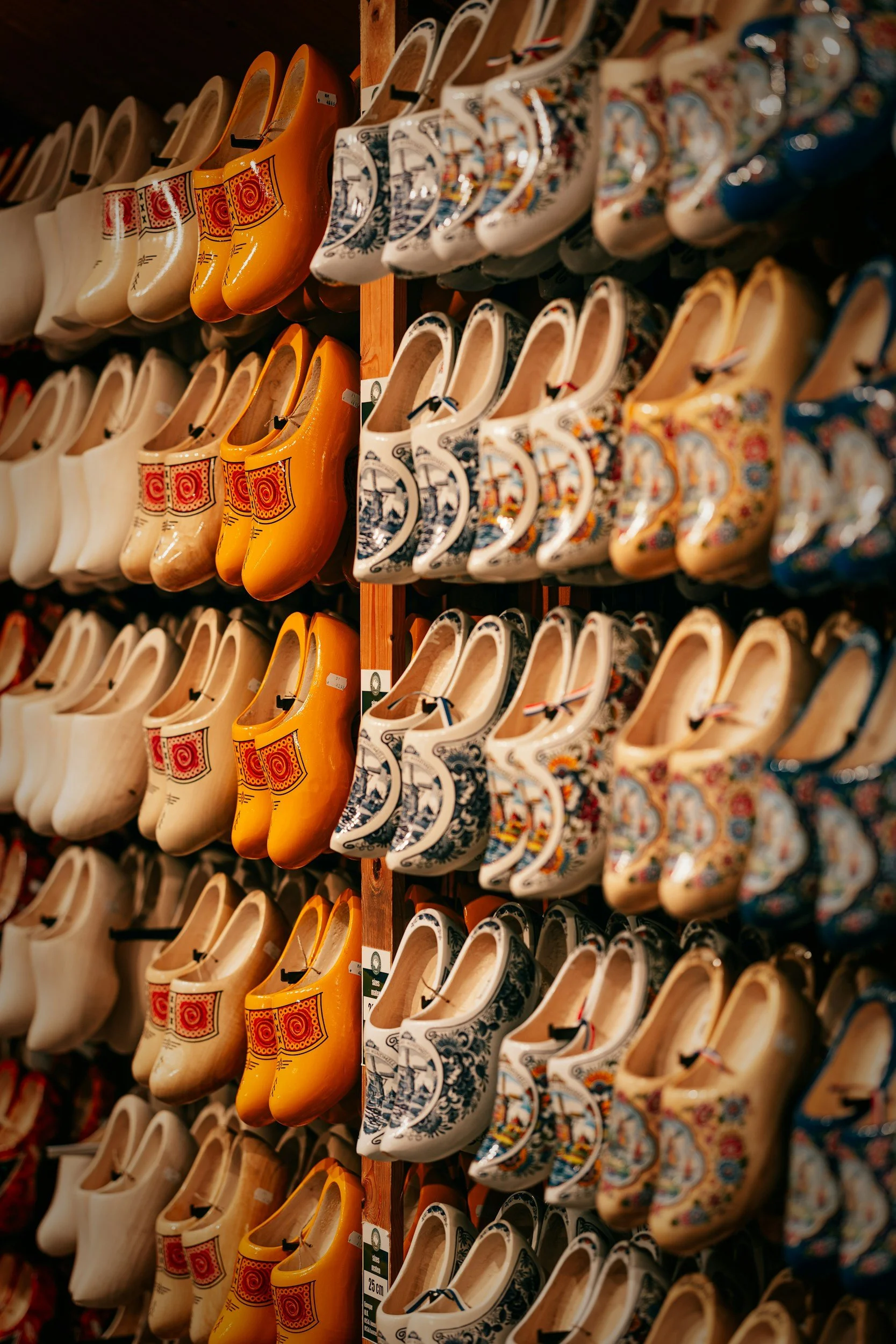 Display of traditional Dutch clogs in various colors and patterns on a wall in a store.