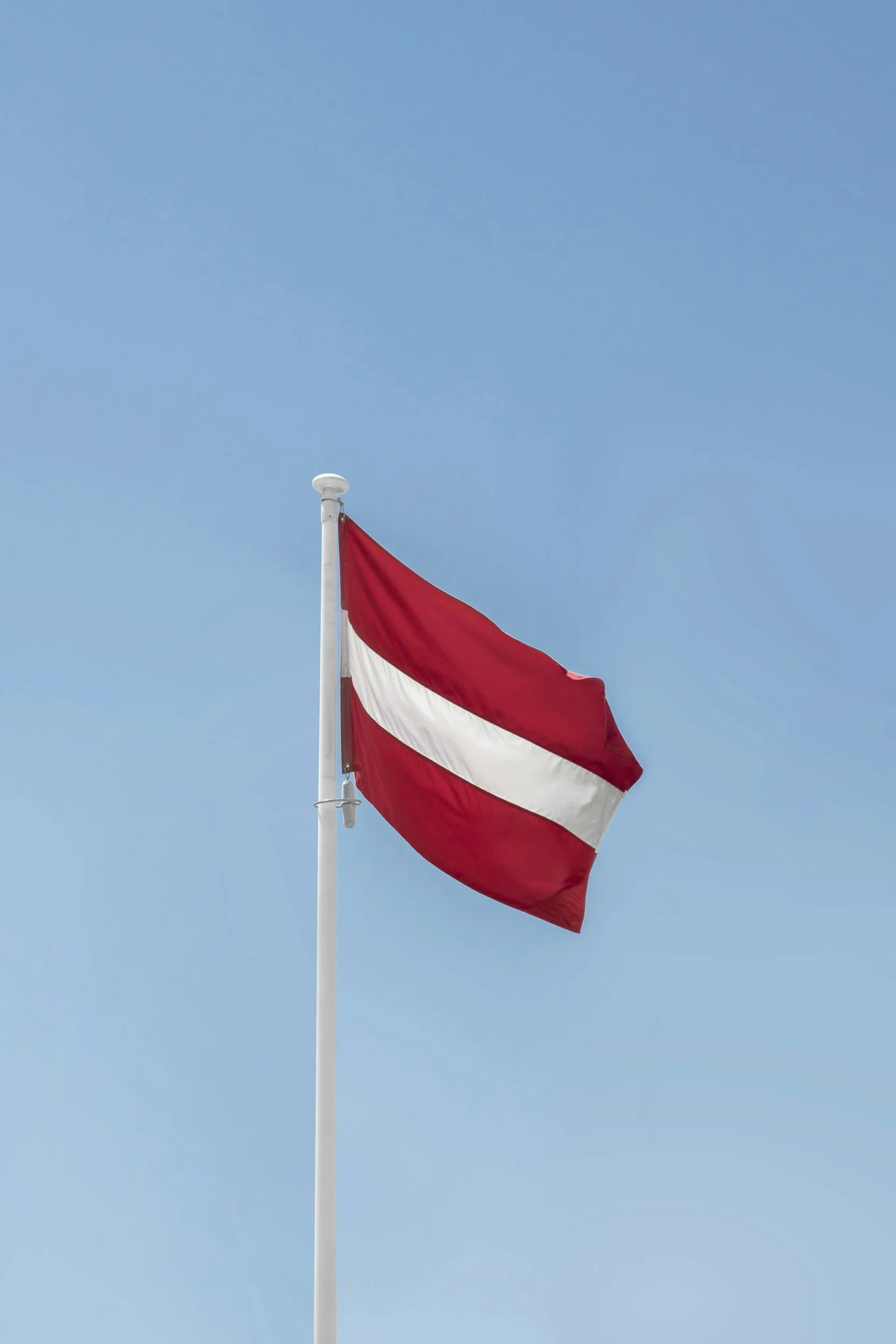 Latvian flag flying on a flagpole against a clear blue sky.