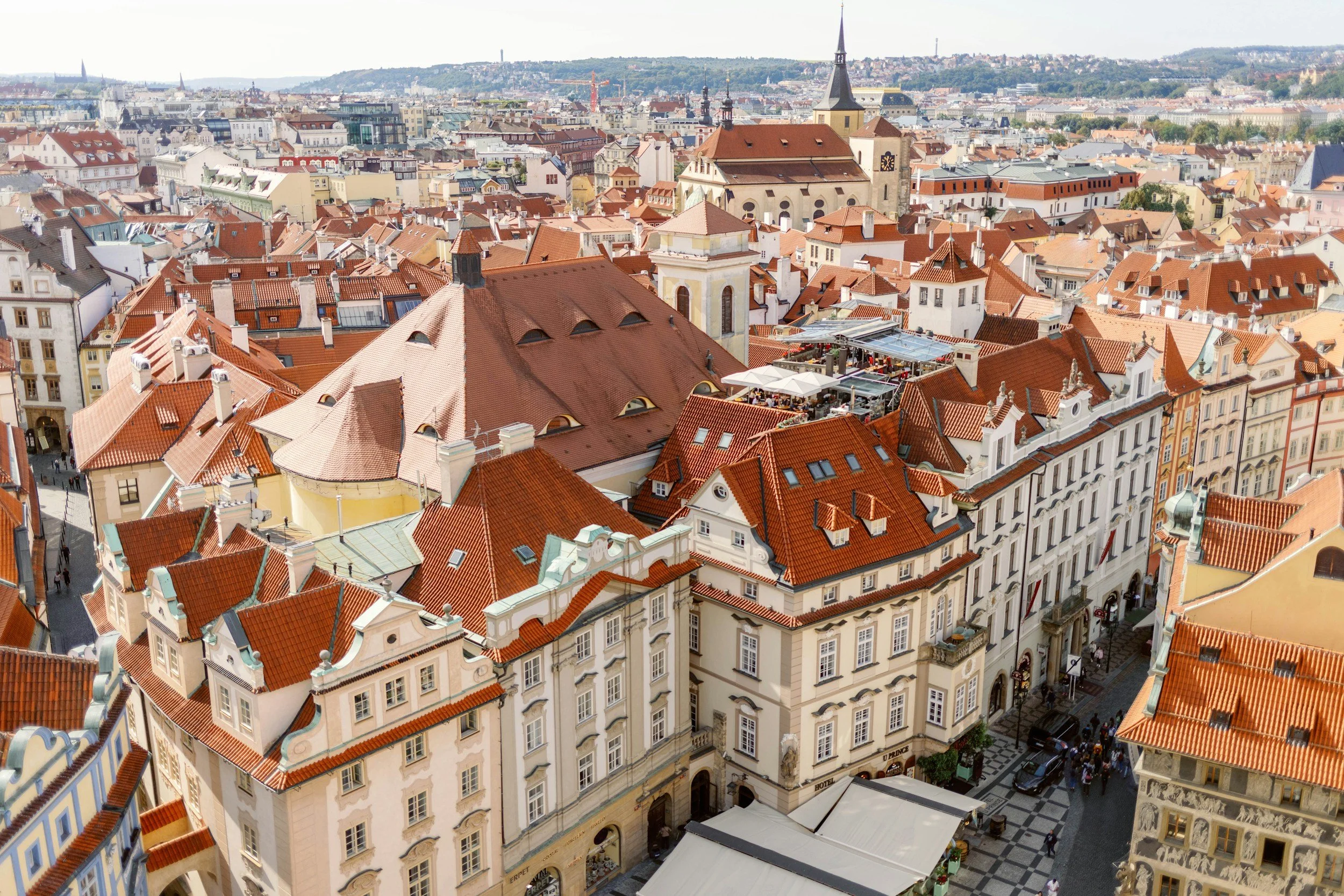 Aerial view of Prague, Czech Republic, showing historic buildings with red rooftops and a city street filled with pedestrians.