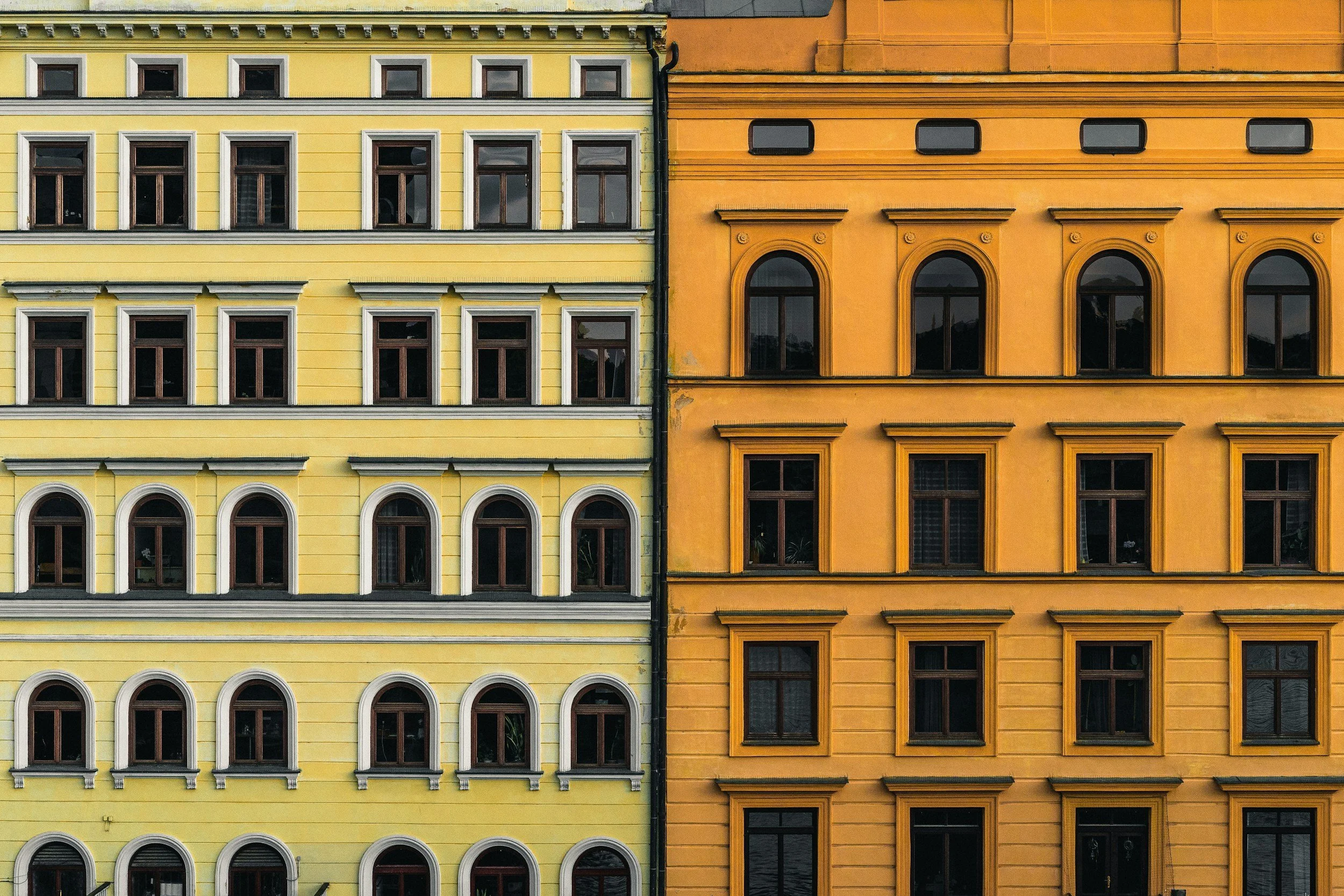 Close-up of colorful European apartment buildings with yellow and orange facades, multiple windows, and ornate architectural details.
