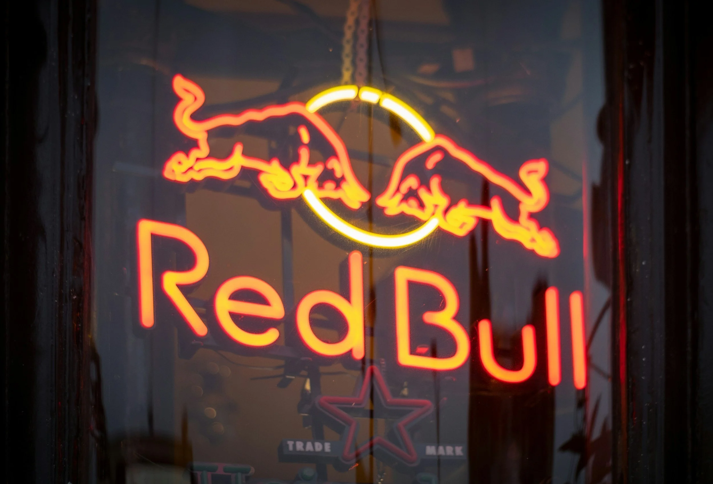 Neon sign of two red bulls charging at each other with a yellow circle between them and the words 'Red Bull' below in red lettering.