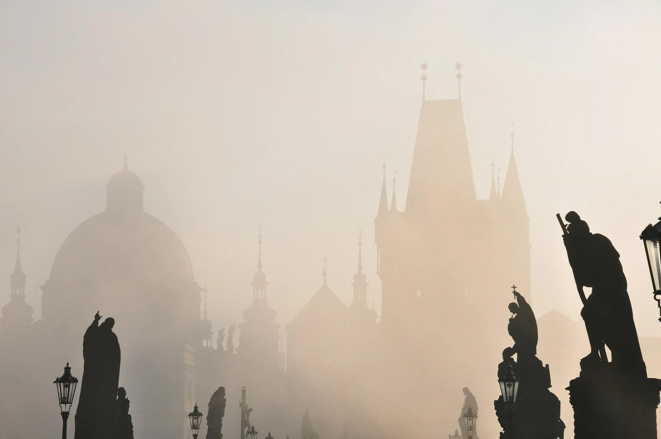 Silhouettes of statues and historic buildings in foggy Prague, Czech Republic, during daytime