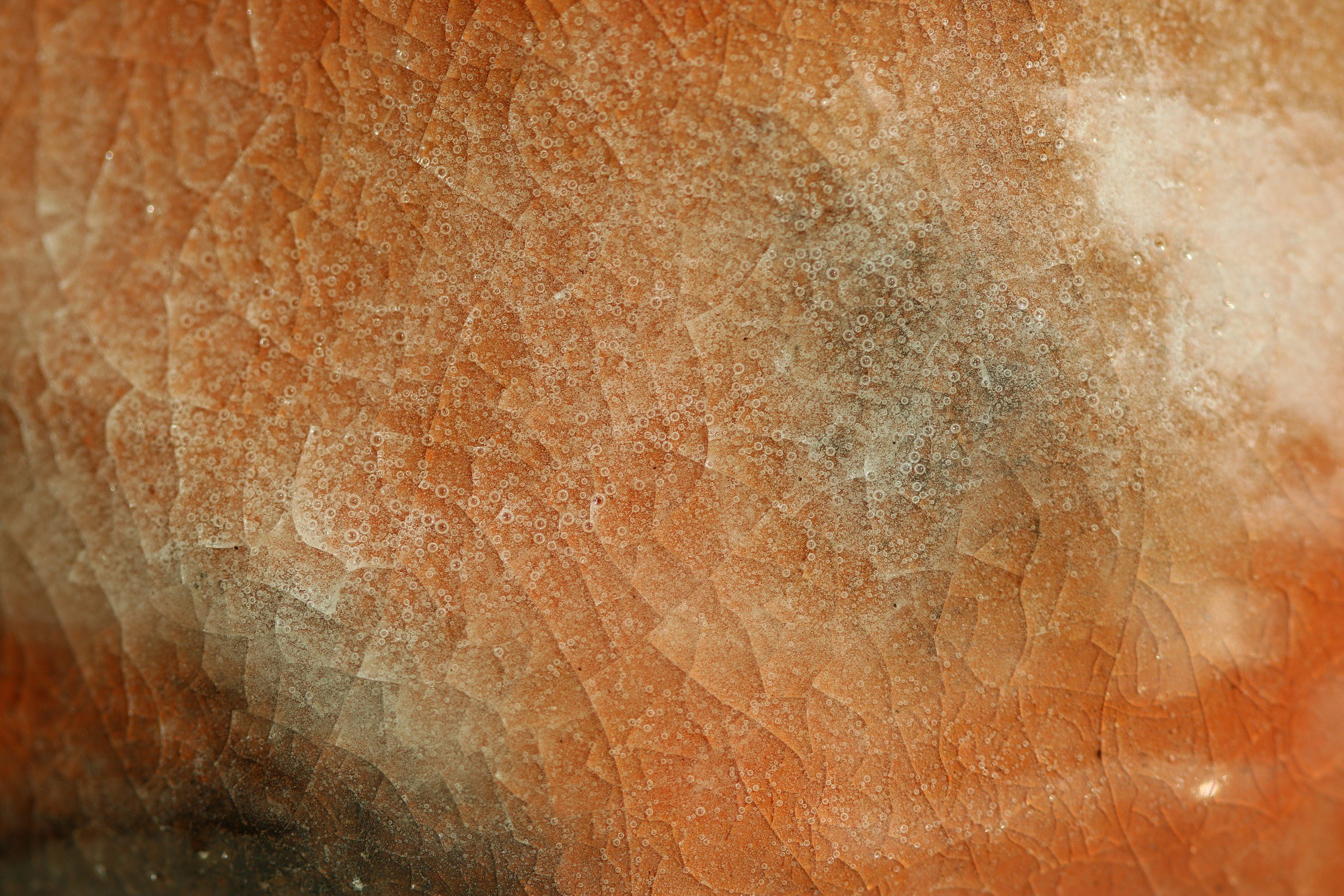 Close-up of a frozen, icy surface with cracks and bubbles, in shades of beige and orange.