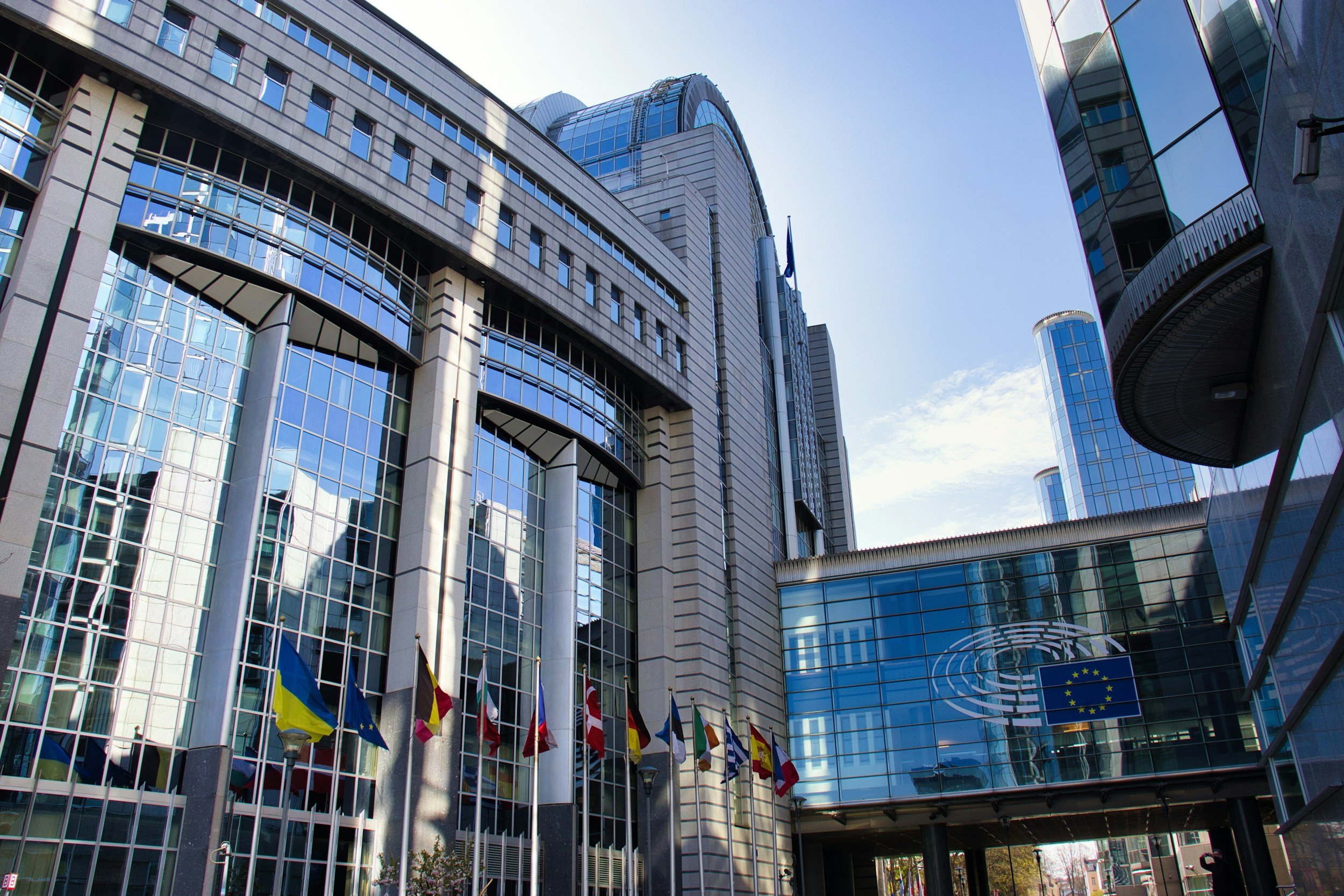 European Parliament building with flags, glass windows, and blue sky