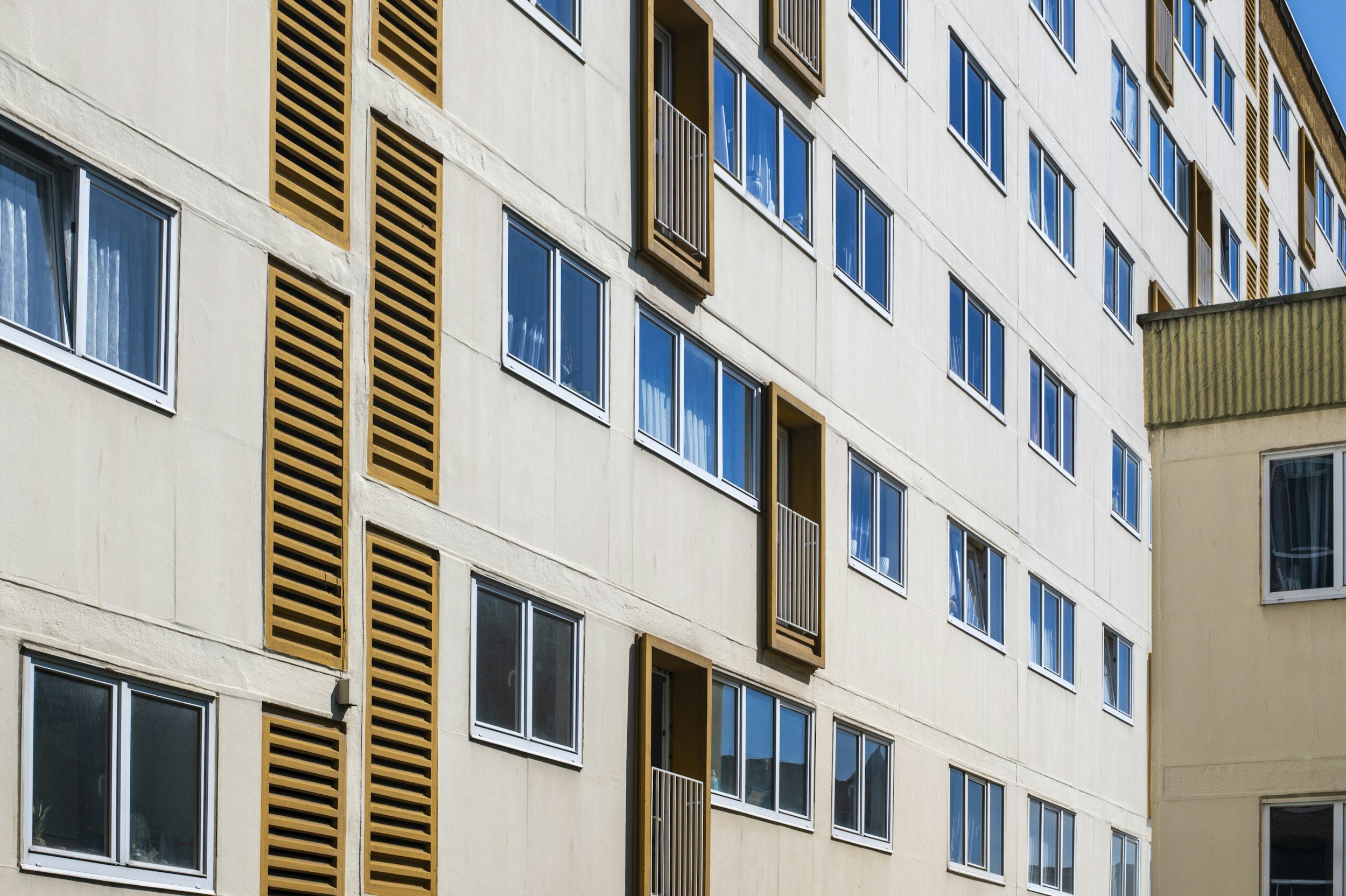 Exterior view of a modern multi-story apartment building with numerous windows and some balconies, with another building partially visible on the right.