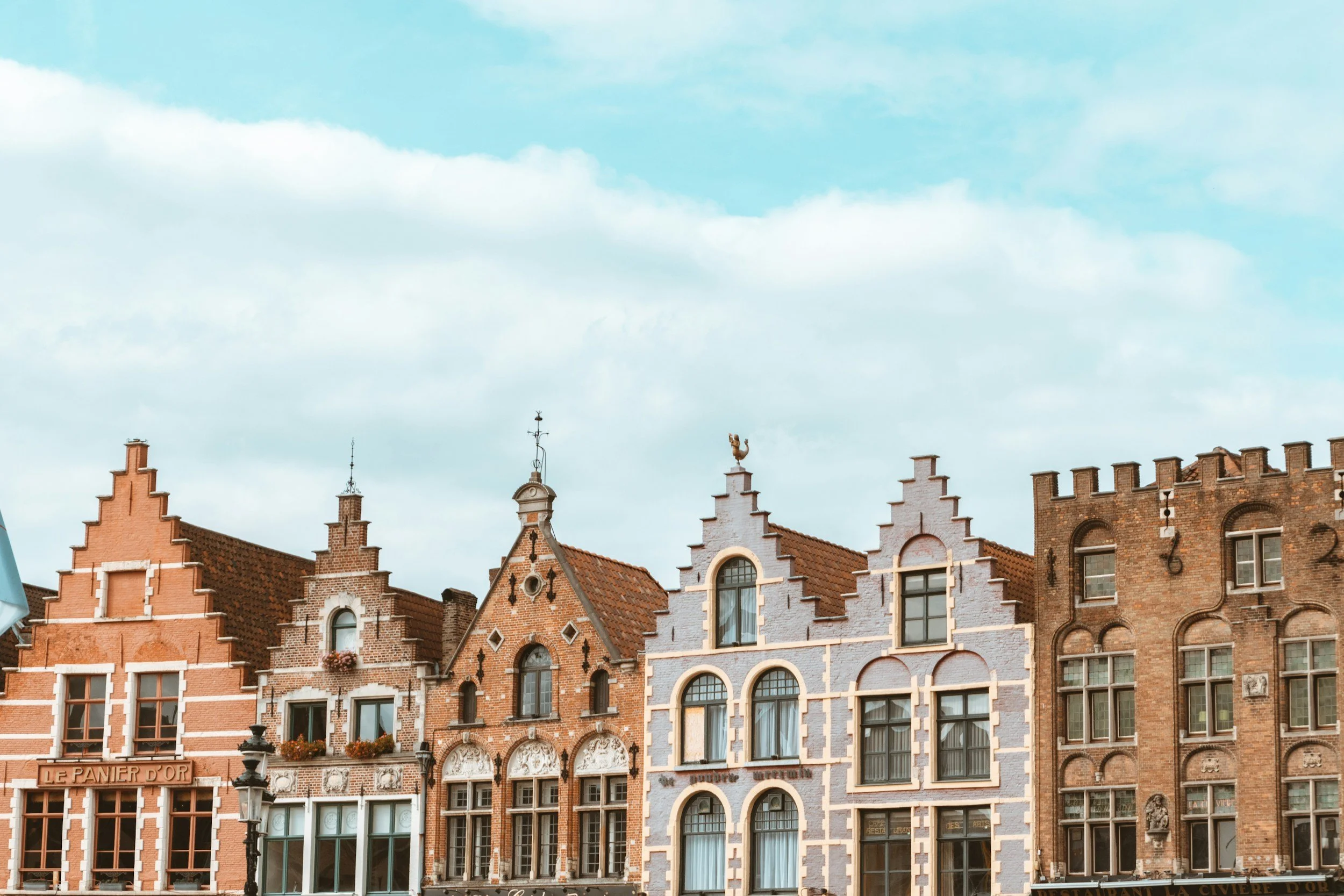 Row of historic European-style buildings with ornate facades, gabled roofs, and decorative elements under a partly cloudy sky.
