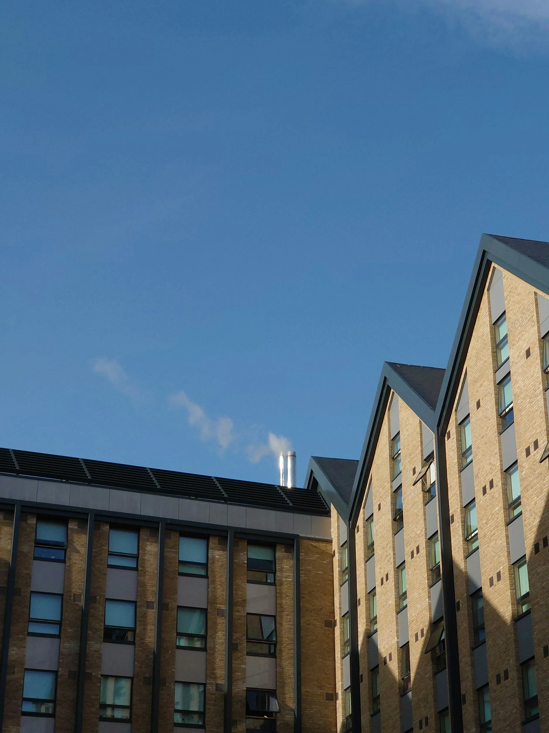 Two modern brick apartment buildings with pitched roofs and multiple windows under a clear blue sky.