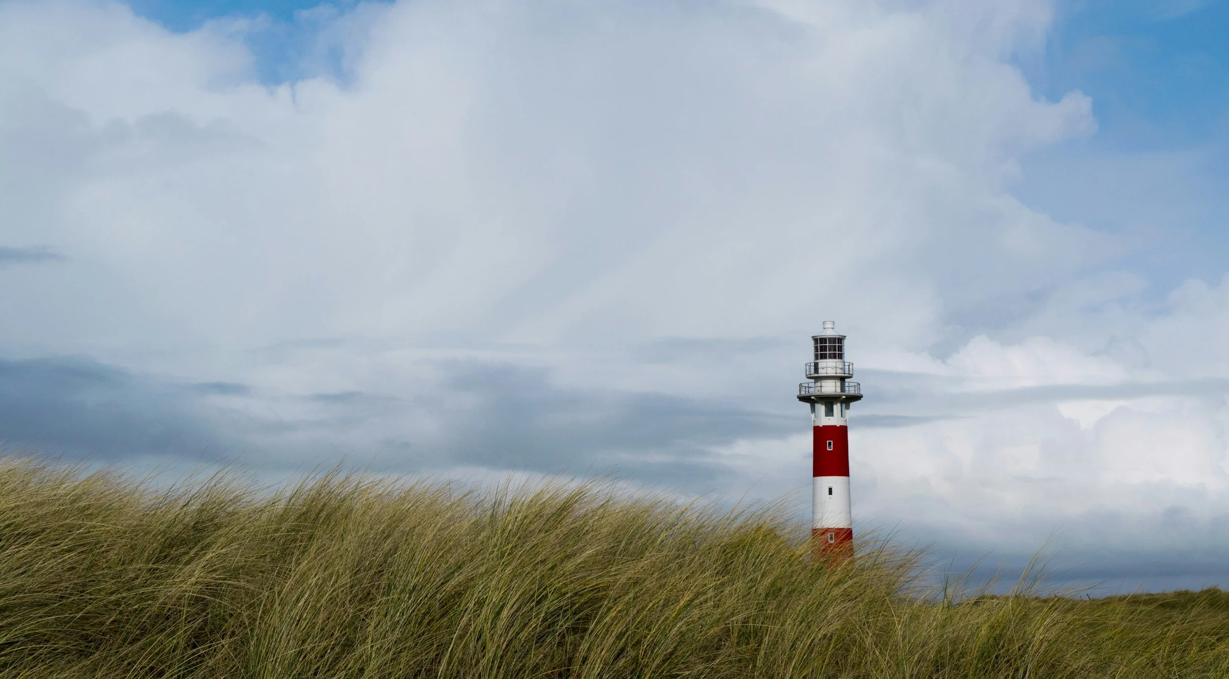 A lighthouse on a grassy coastal area with cloudy sky in the background.