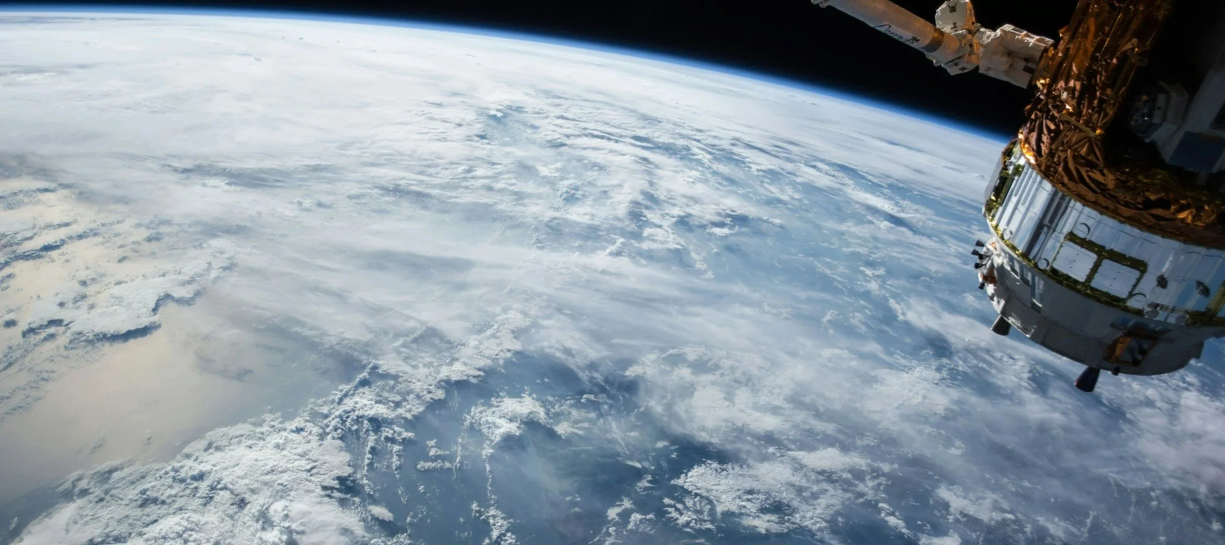 View of Earth from space showing clouds and the horizon, with part of a spacecraft visible on the right side.