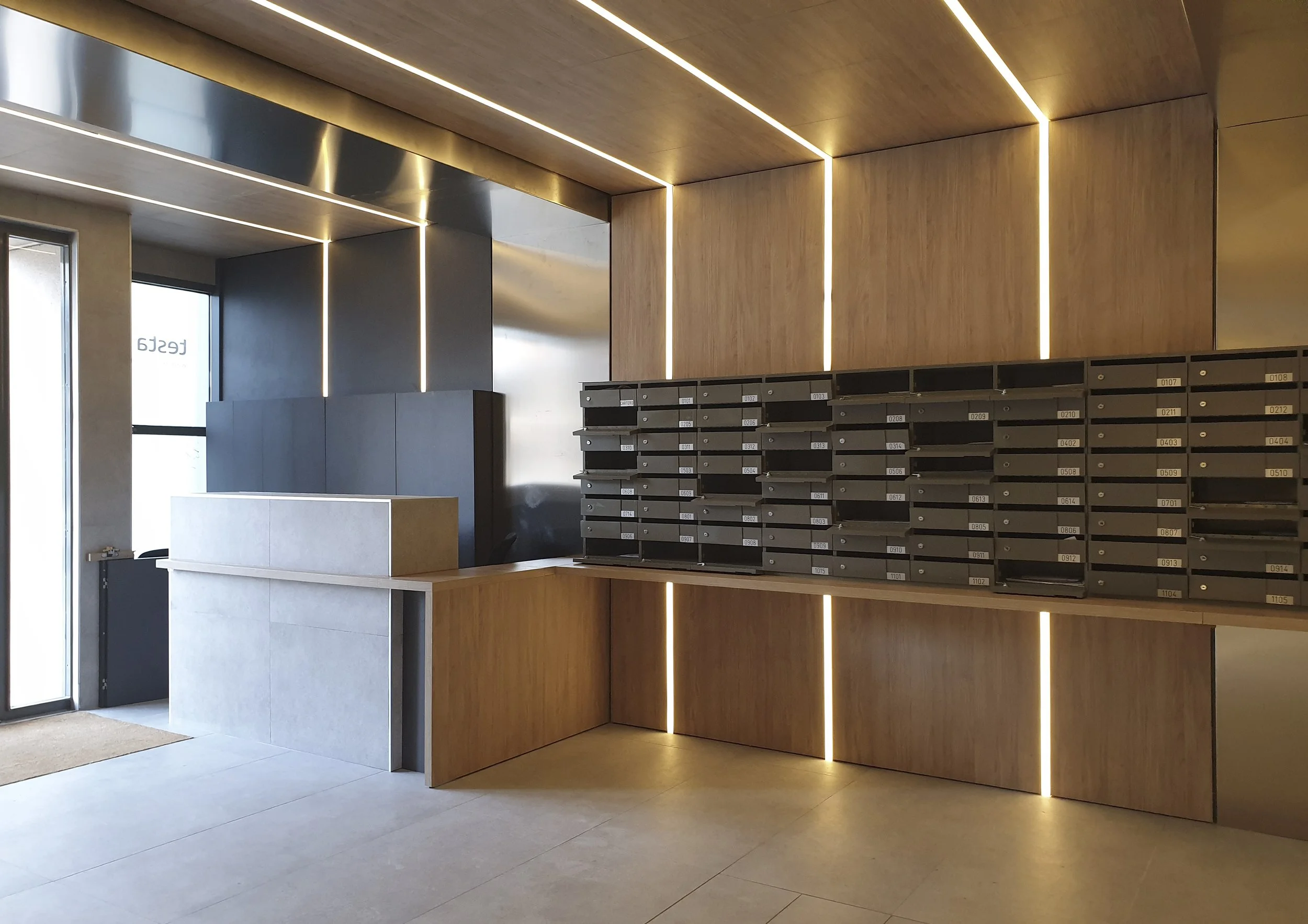 Recepción moderna con madera en las paredes y luz LED, buzones de correo en primer plano, puerta de entrada de vidrio en el fondo.