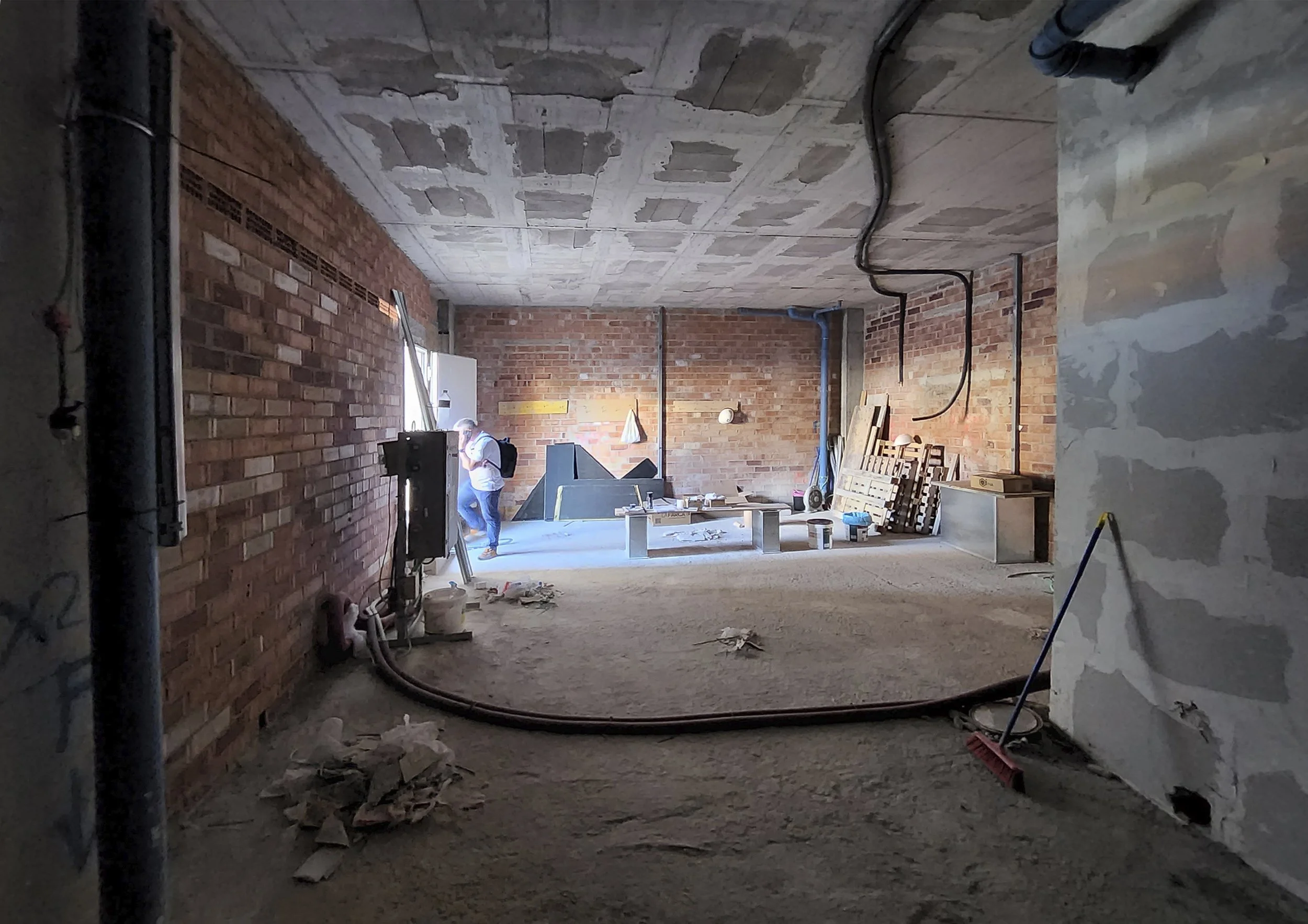Interior de una construcción en proceso con paredes de ladrillo y un techo de cemento, y una persona trabajando en el sitio.