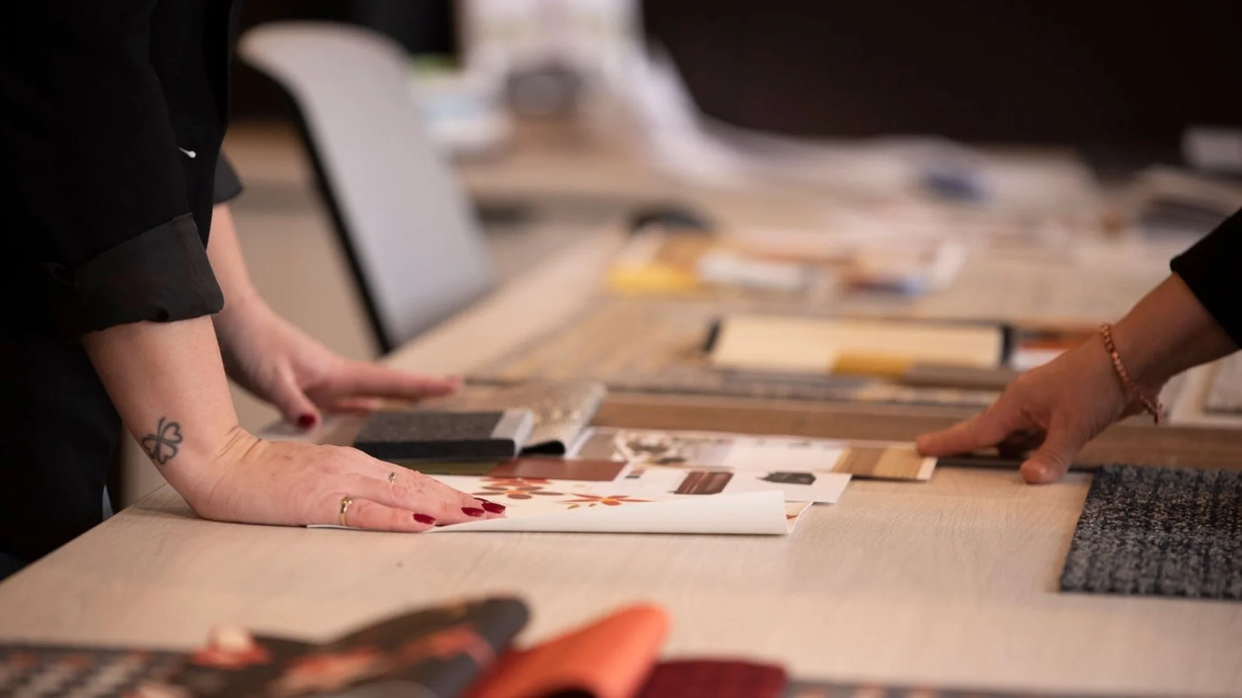 Two people are looking at fabric and material samples on a table, with various fabric swatches, papers, and swatches spread out.