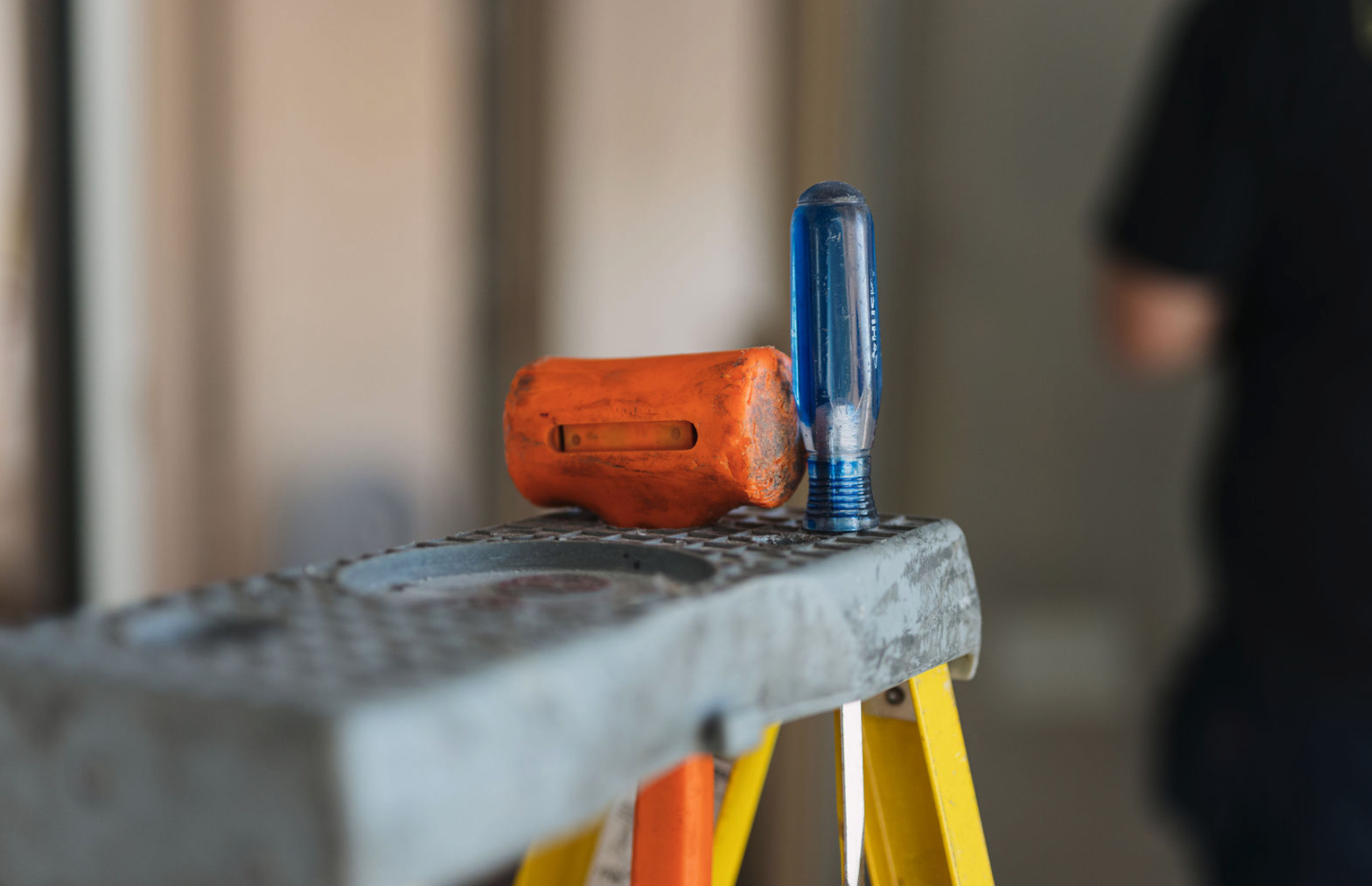 A blue flashlight and an orange flashlight resting on a gray step ladder.
