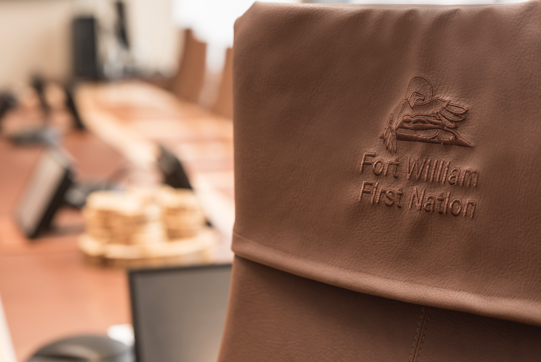 Close-up of a brown leather chair with an embossed logo and text that reads 'Fort William First Nation' in a meeting or conference room.