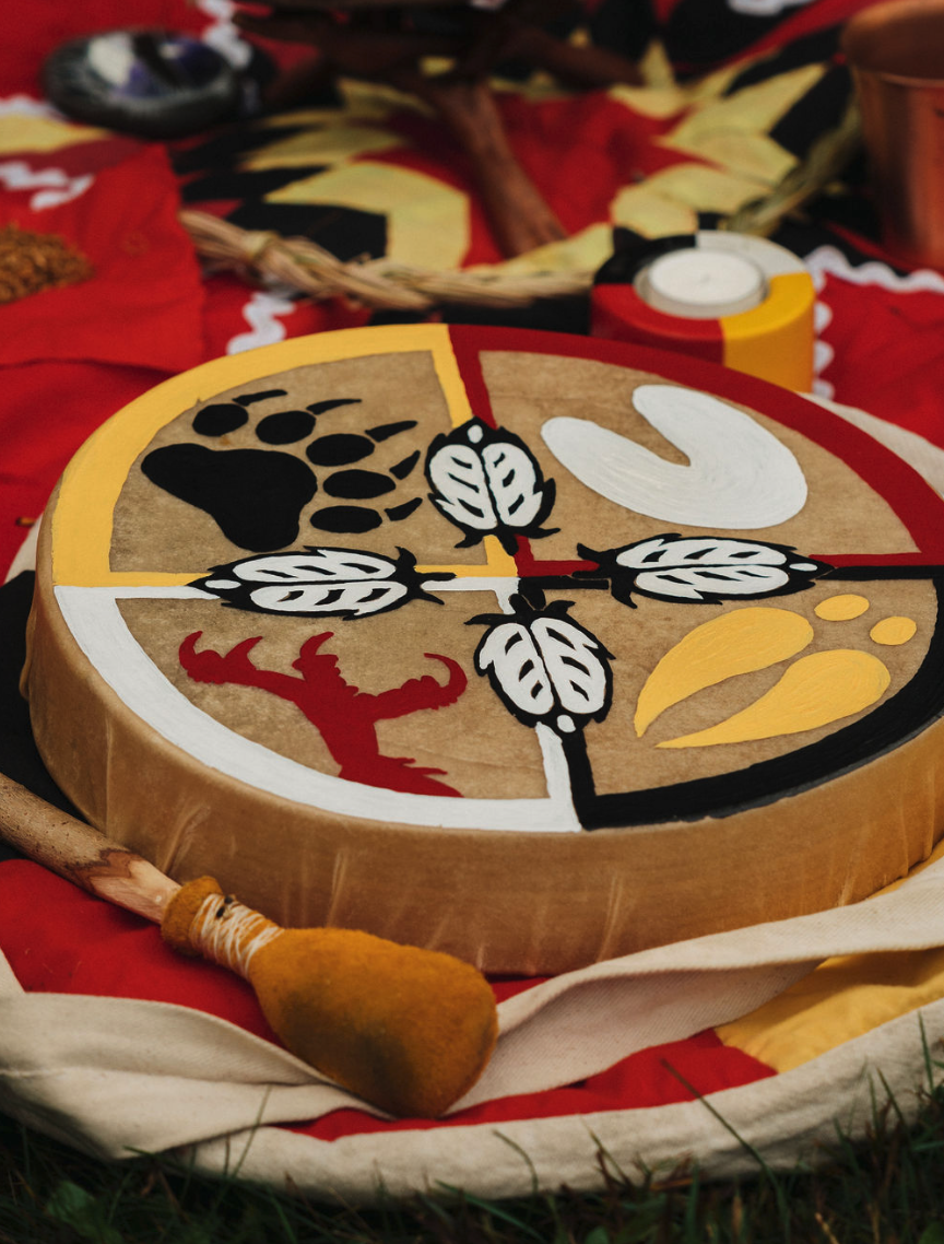 Painted circular wooden plaque with four quadrants featuring African wildlife and cultural symbols, surrounded by traditional-themed decor and a gourd-shaped rattle.