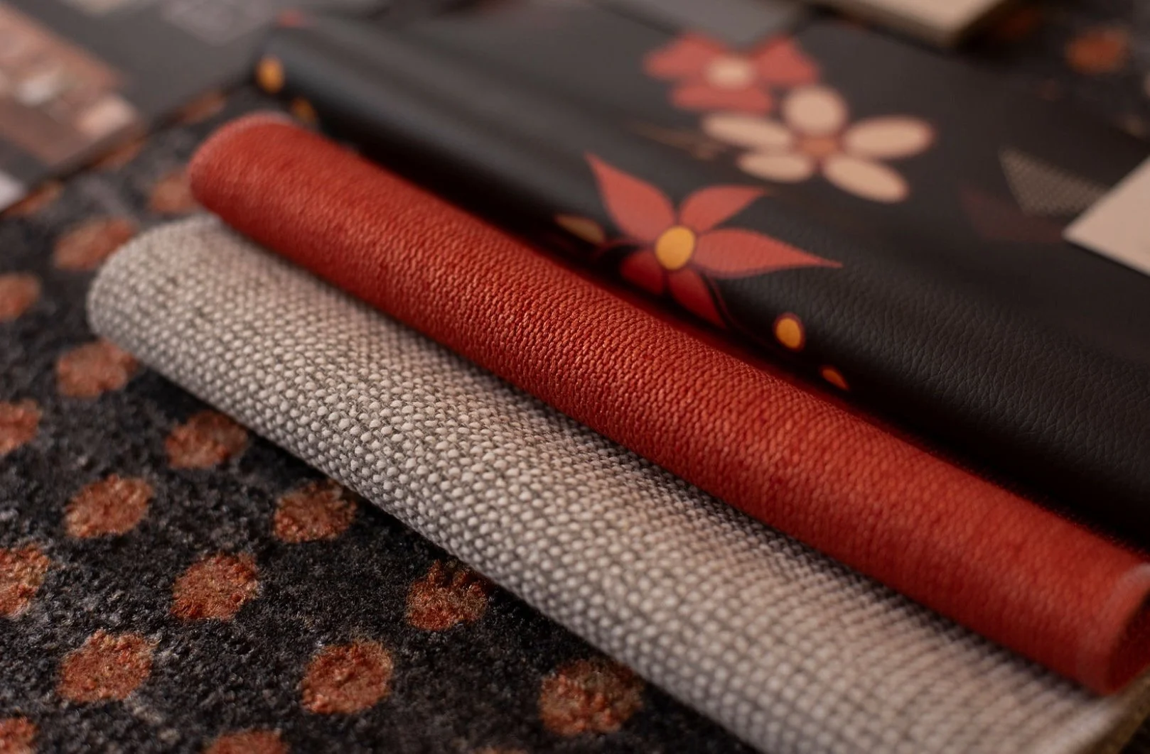 Close-up of three folded fabric samples in gray, red, and beige colors, resting on a textured dark background.