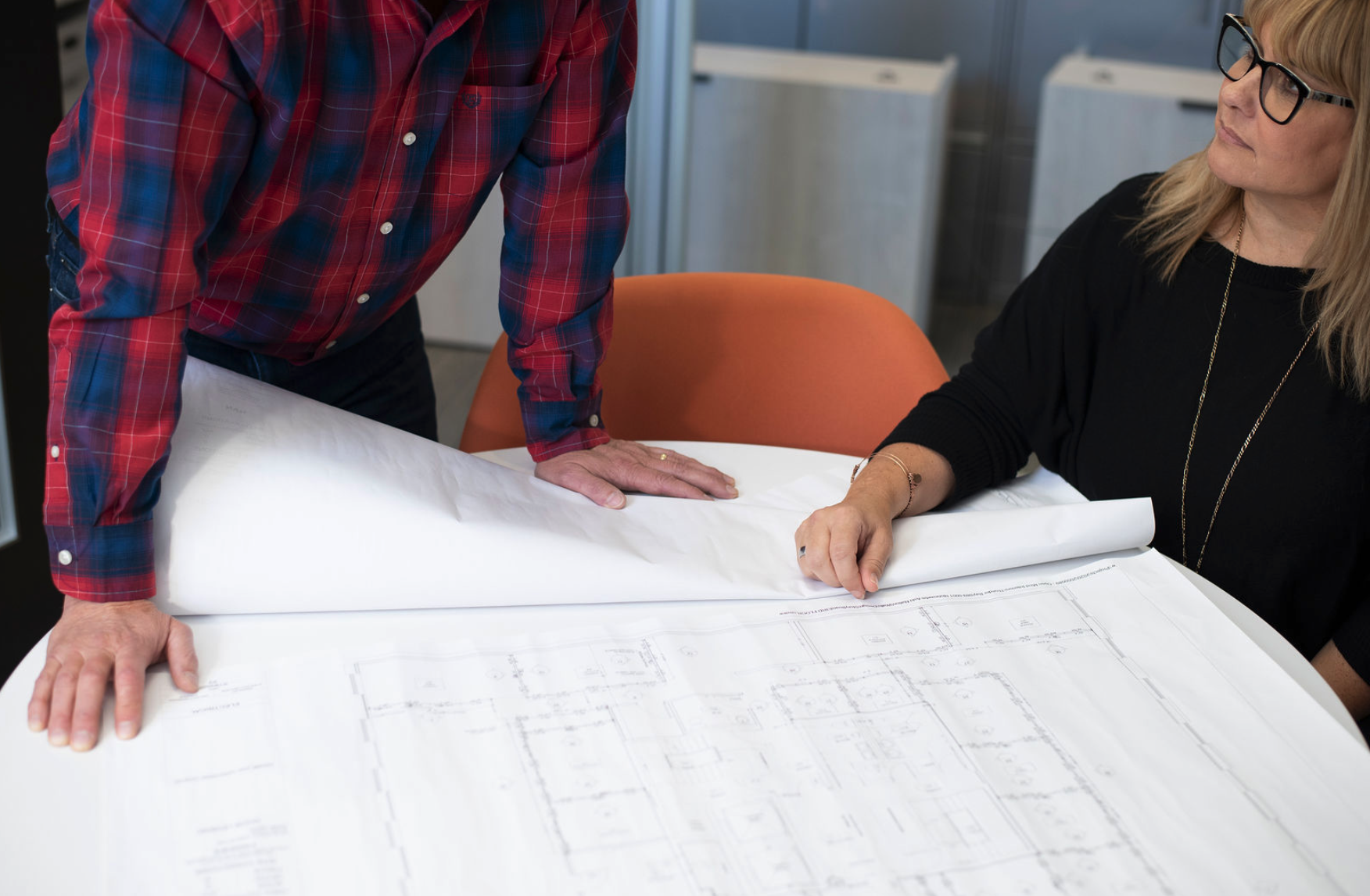 Two people reviewing architectural plans on a table in an office.