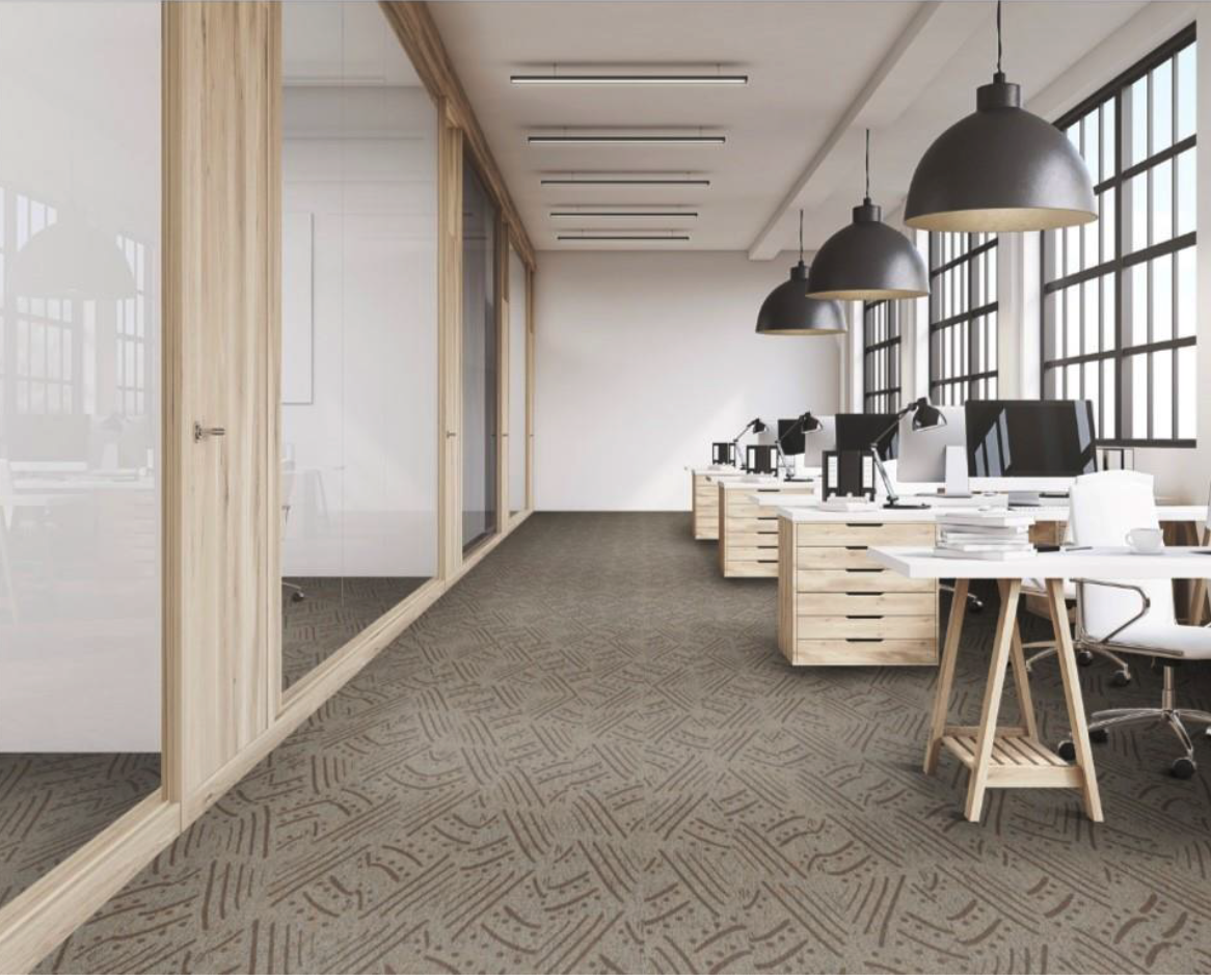 Modern office space with workstations, desks, and chairs. Large windows with black frames allowing natural light. Pendant lights hanging from the ceiling, wooden accents, and glass-walled meeting rooms on the left.