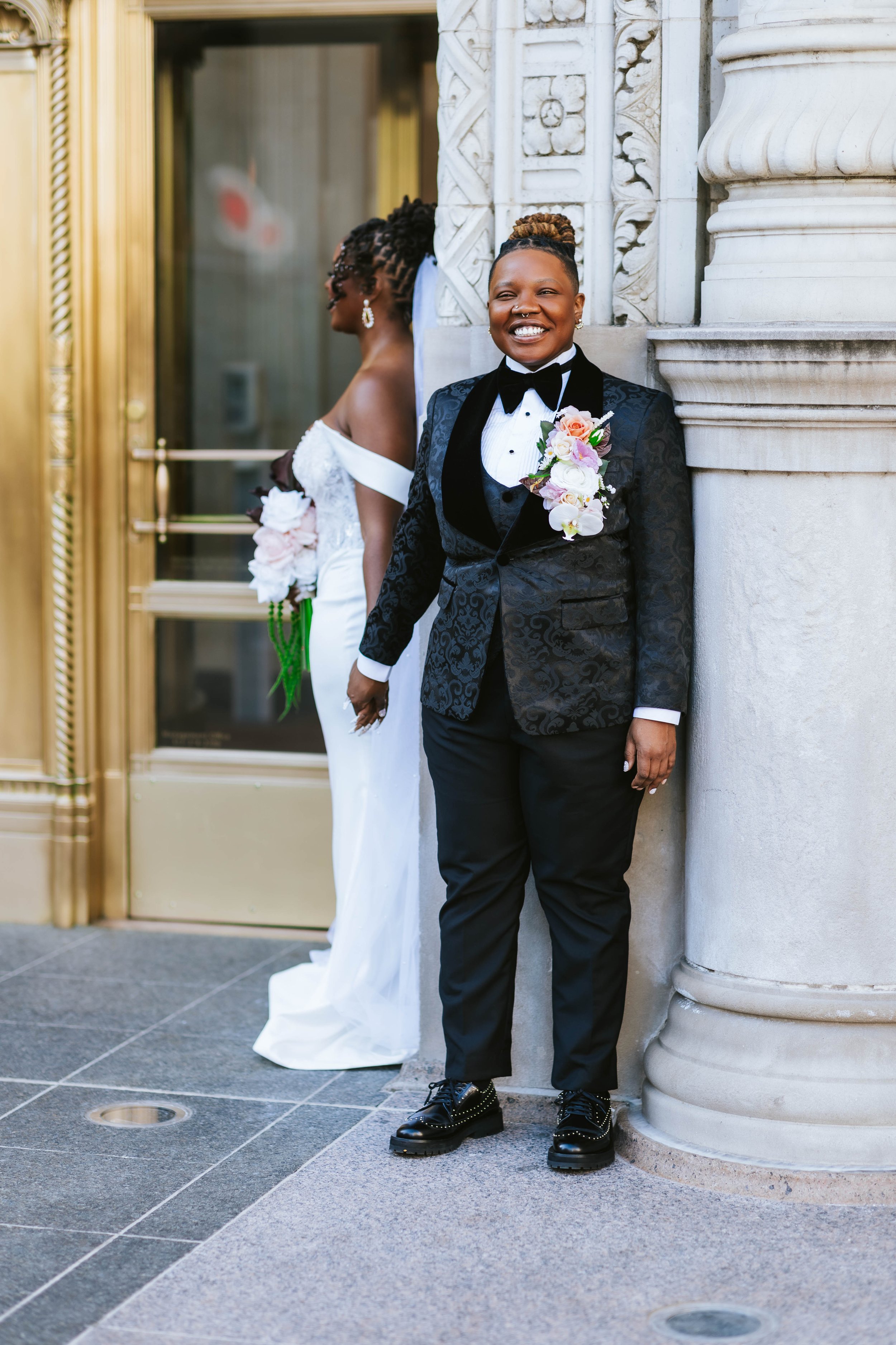 Hand holding a faux wedding bouquet of white roses and small white flowers with green leaves and a white ribbon against a plain light background for wedding savings
