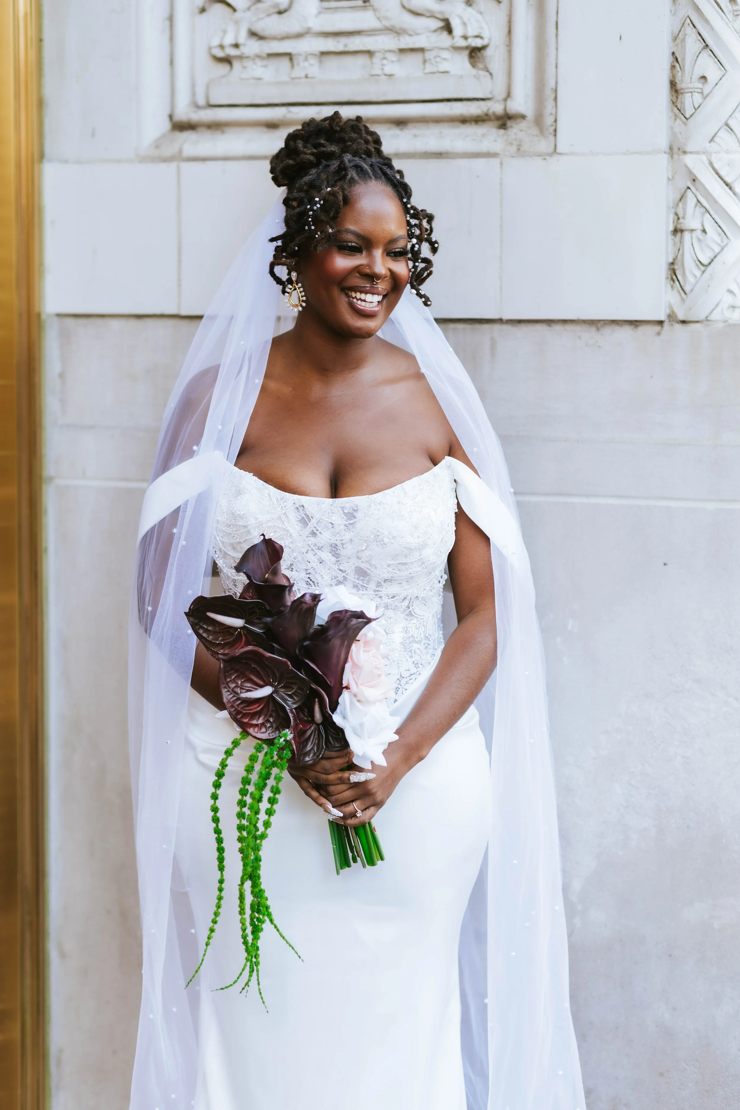 Person holding a wedding bouquet in Chicago of white and gold artificial flowers with green leaves against a plain background.