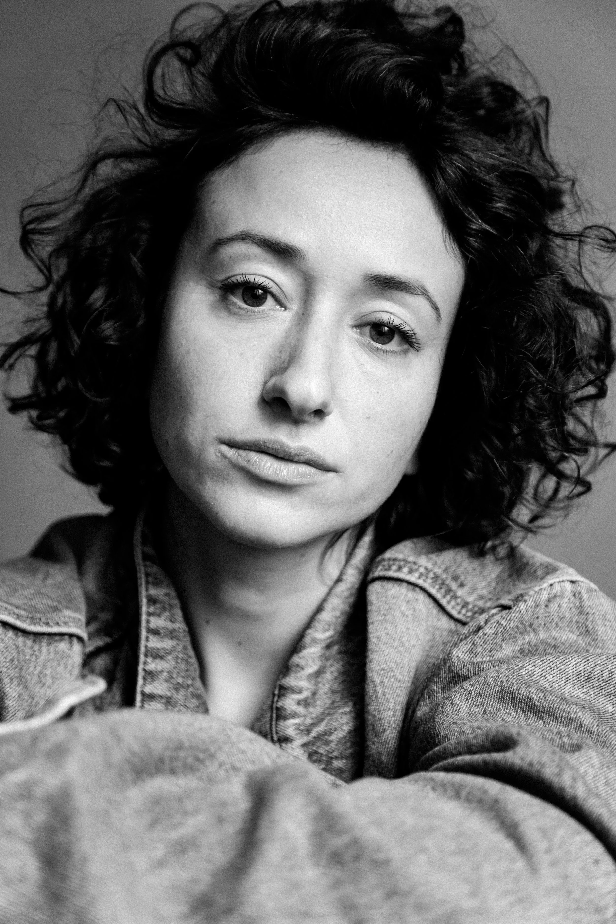 Portrait en noir et blanc d'une jeune femme avec des cheveux bouclés, portant une veste en jean.