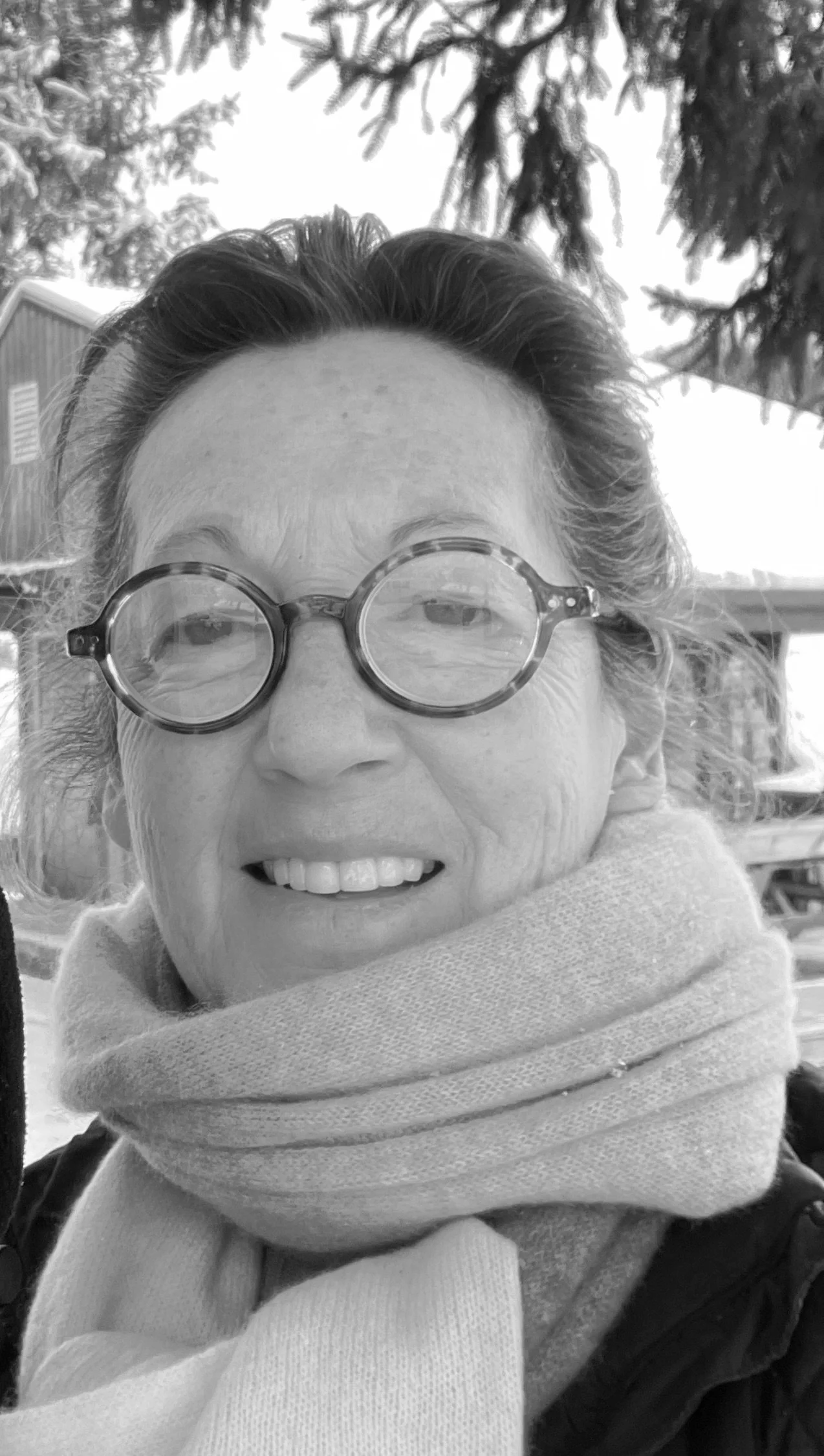 Black-and-white portrait of a woman, cofounder of Conscious Evolution Dialogues, wearing round glasses and a scarf outdoors.