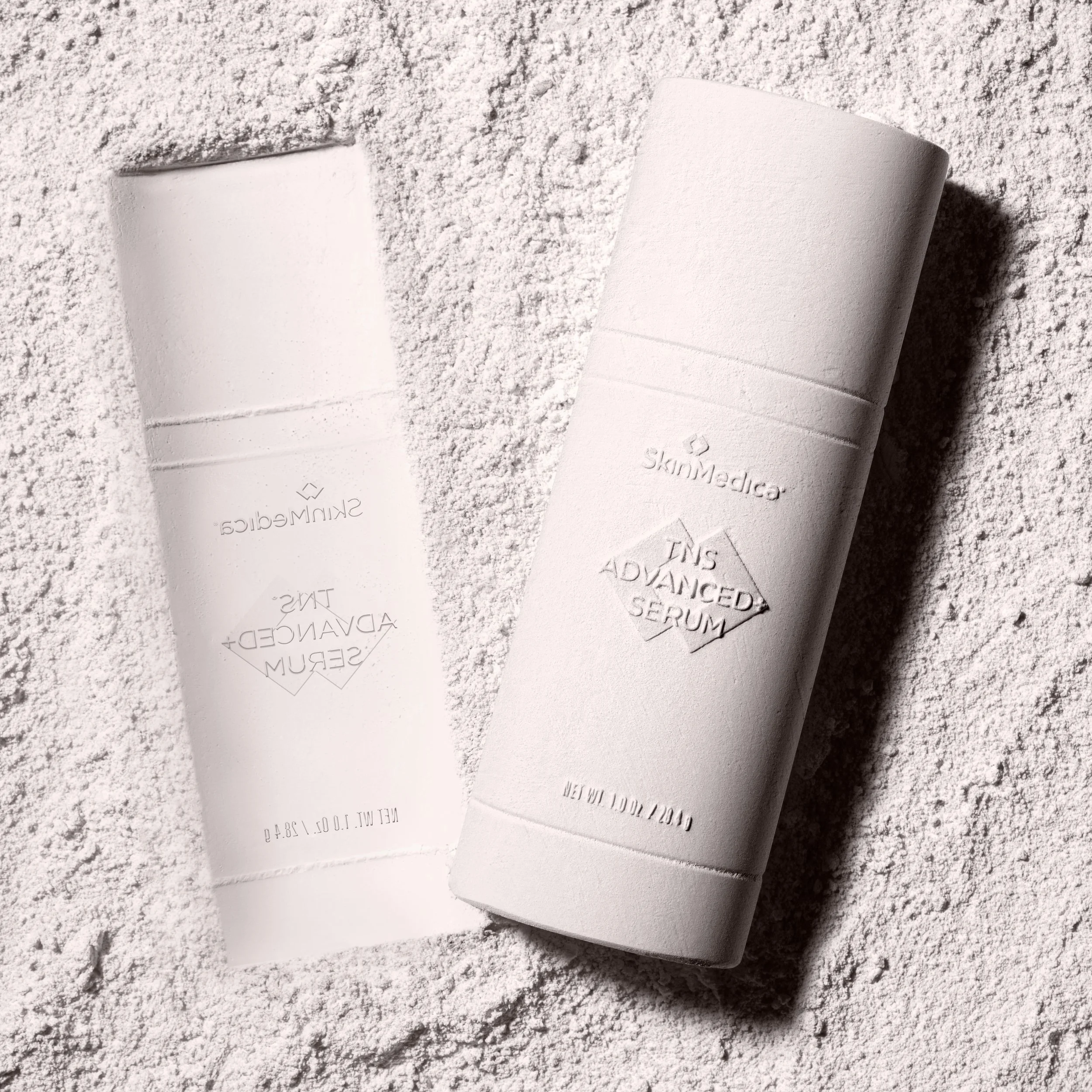A white cylindrical skincare product container and a white rectangular card with embossed text, placed on a textured light-colored surface.