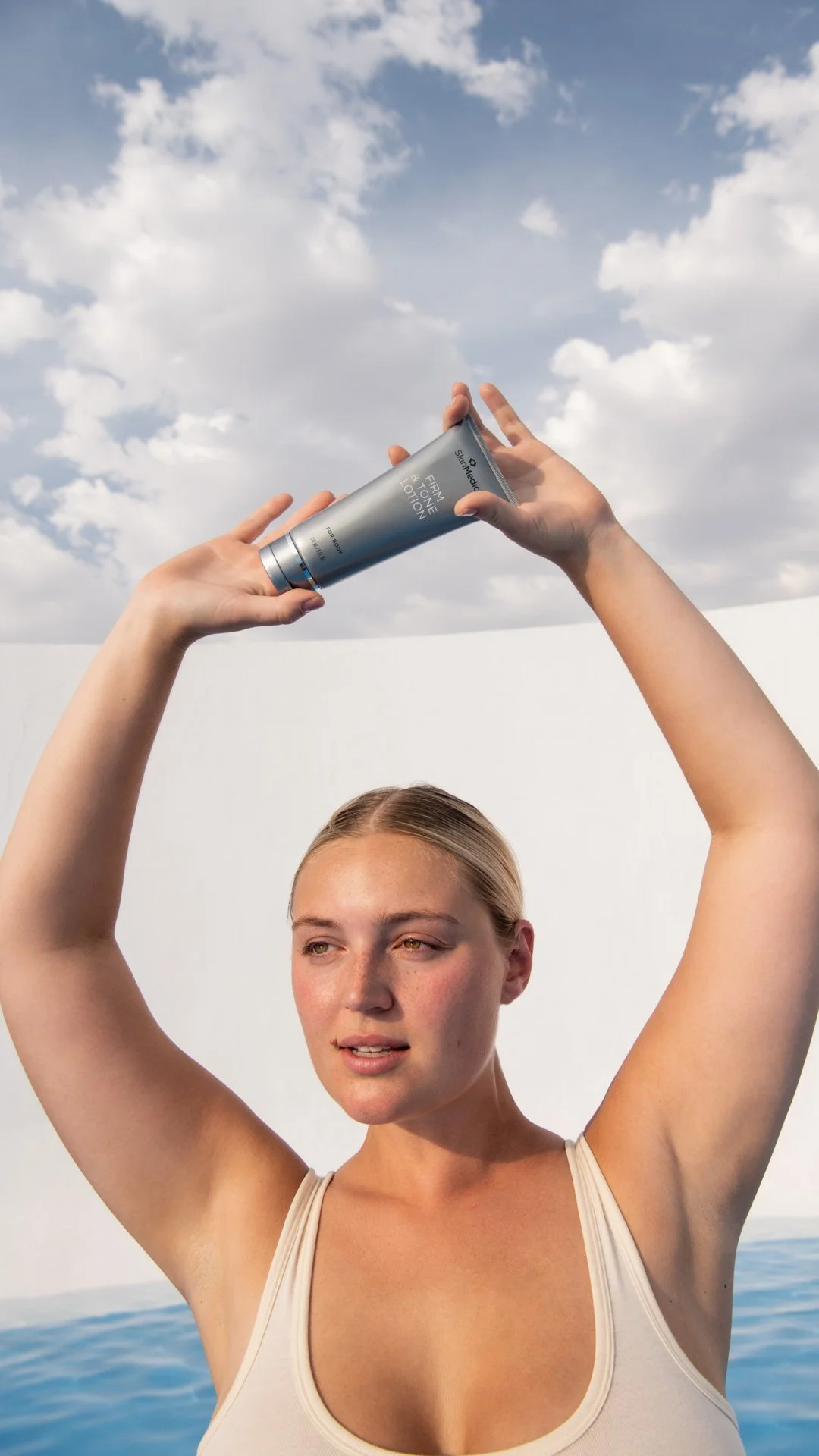 Young woman applying skincare product outdoors with sky and clouds in background.