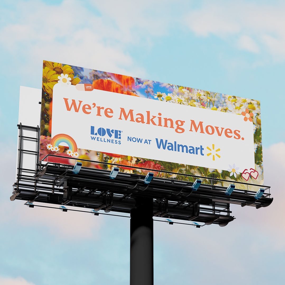 Billboard announcing the opening of Love Wellness at Walmart, with colorful floral and rainbow graphics.