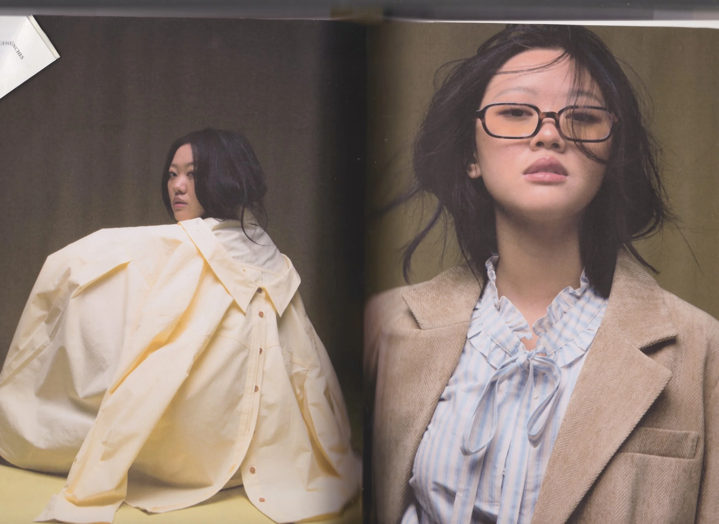 A woman with disheveled hair and glasses wearing a beige blazer over a ruffled, bow-tied blouse.