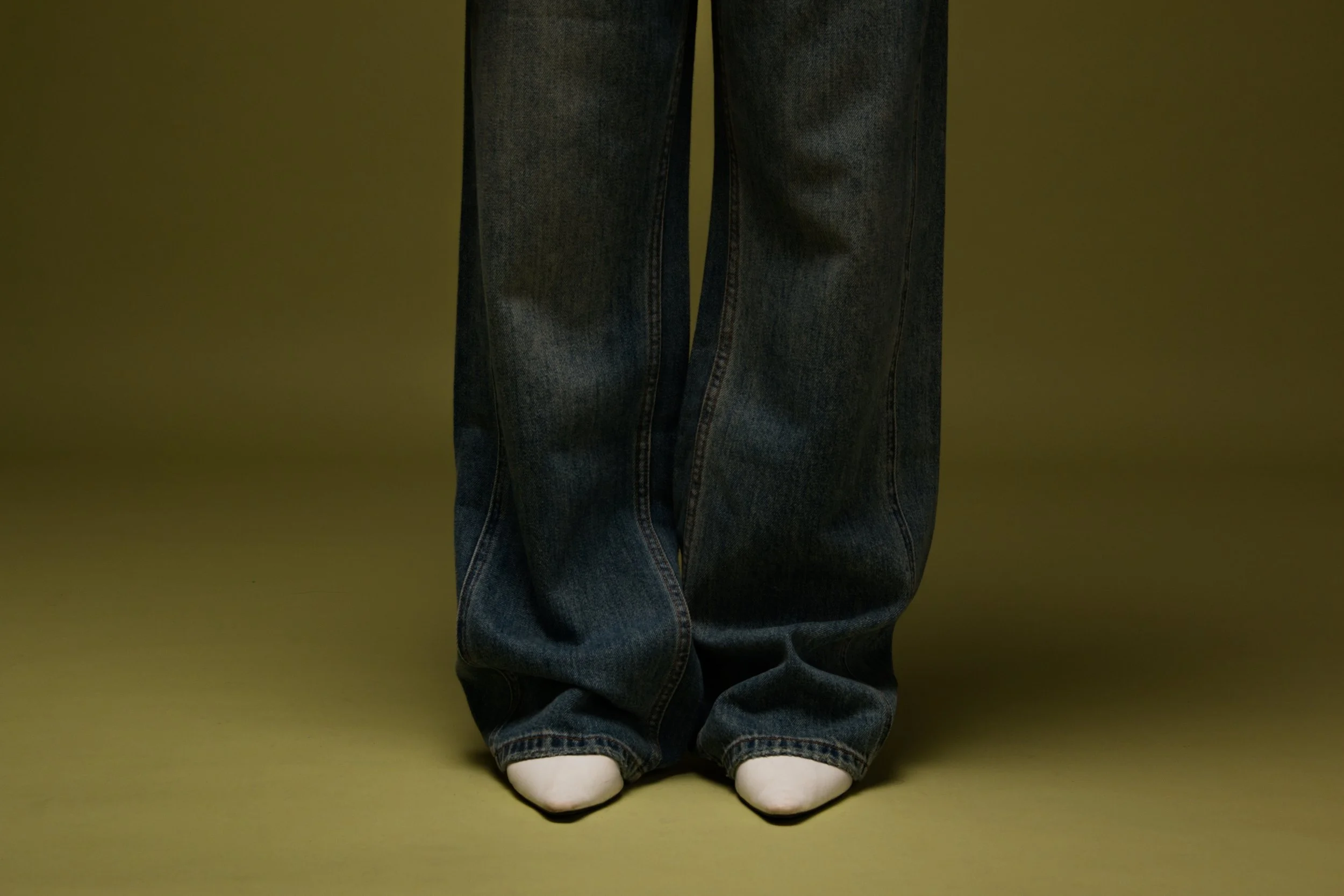 Person standing with wide-leg jeans, wearing white socks, on a solid-colored background.