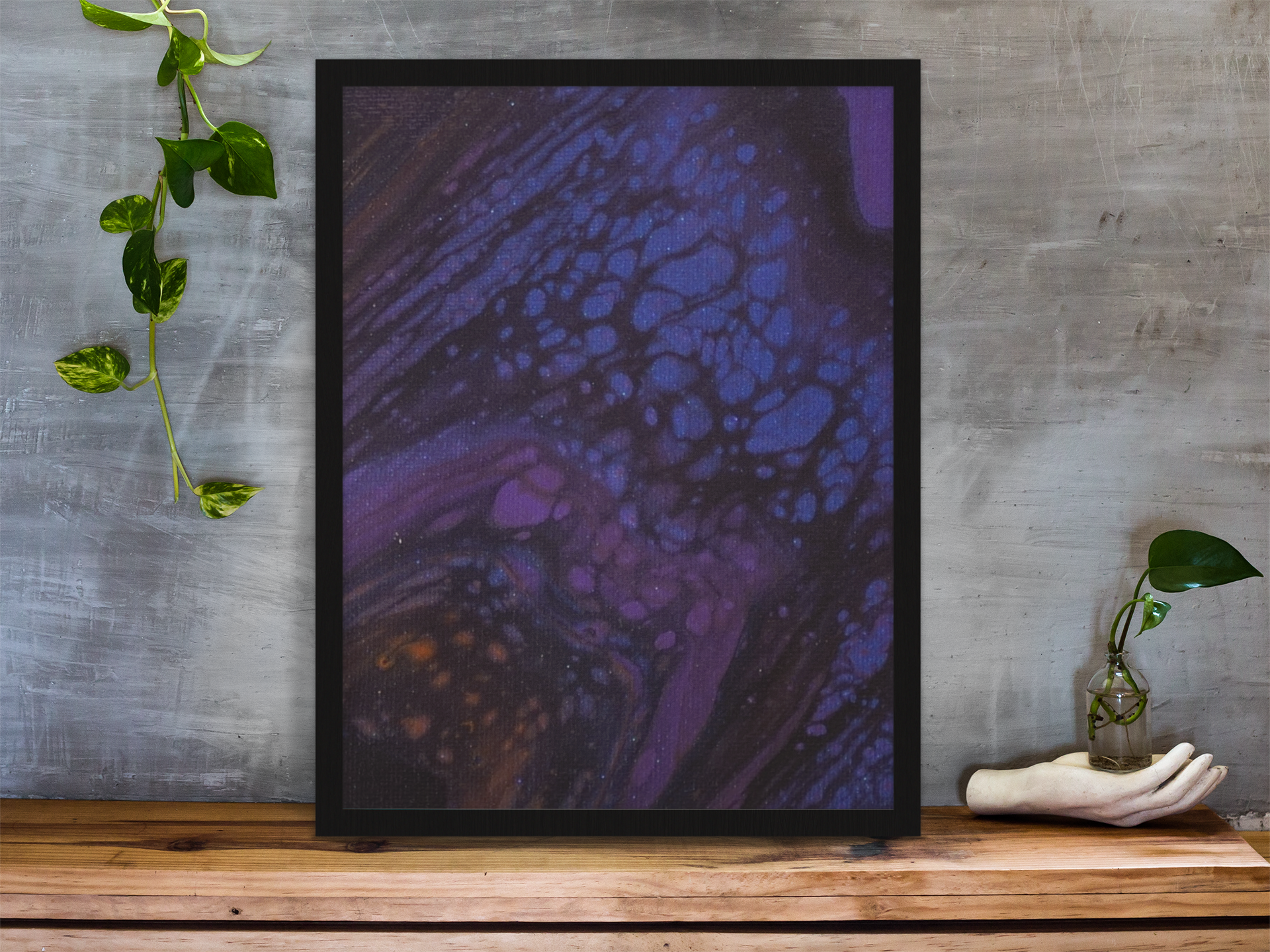 framed-art-print-standing-on-a-wooden-desk-against-a-concrete-wall-near-a-hand-decoration-a10403.png