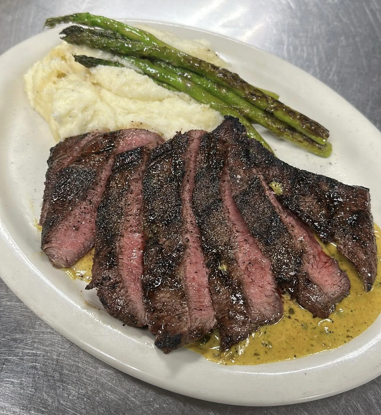 Sliced medium-rare steak with grill marks, accompanied by mashed potatoes and grilled asparagus on a white plate.