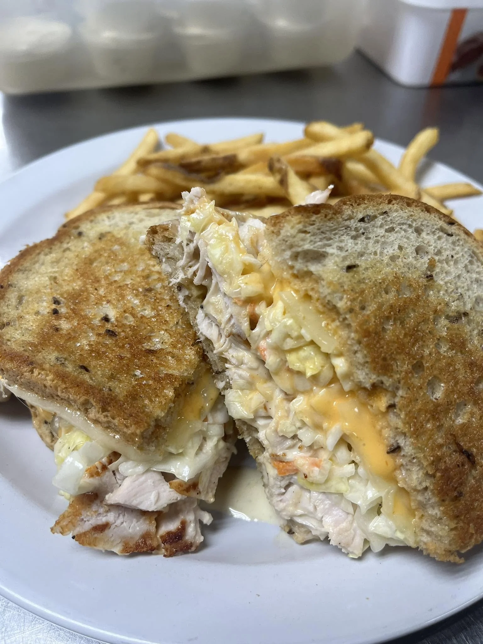 A plate of a partially sliced chicken cordon bleu with melted cheese, alongside French fries on a white plate in a kitchen setting.