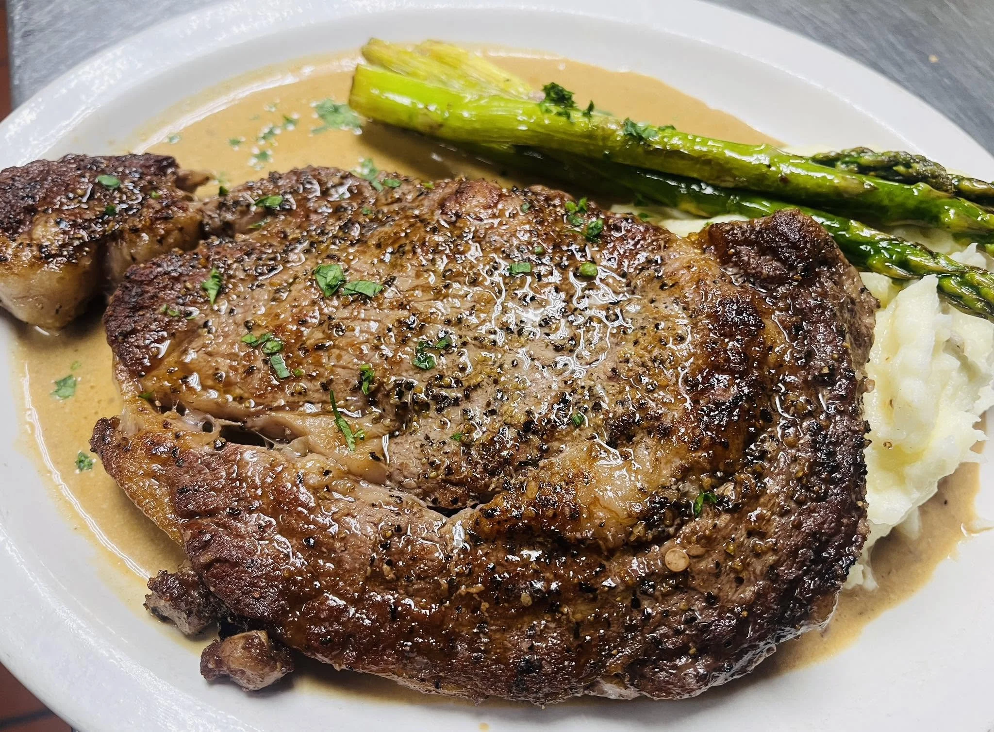 A plate of cooked meat topped with herbs, accompanied by roasted asparagus and mashed potatoes.