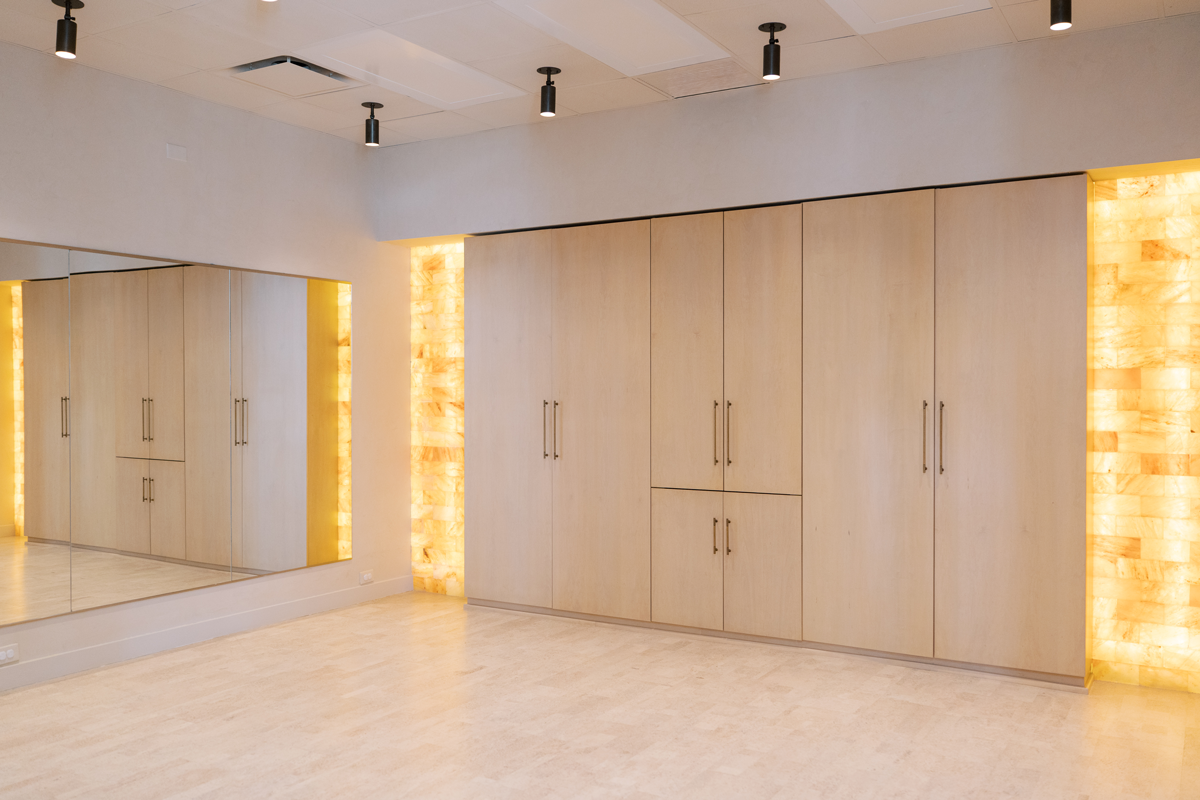 Empty room with beige wooden cabinets, a large mirror on the wall, and salt rock light panels behind the cabinets, with black ceiling spotlights.