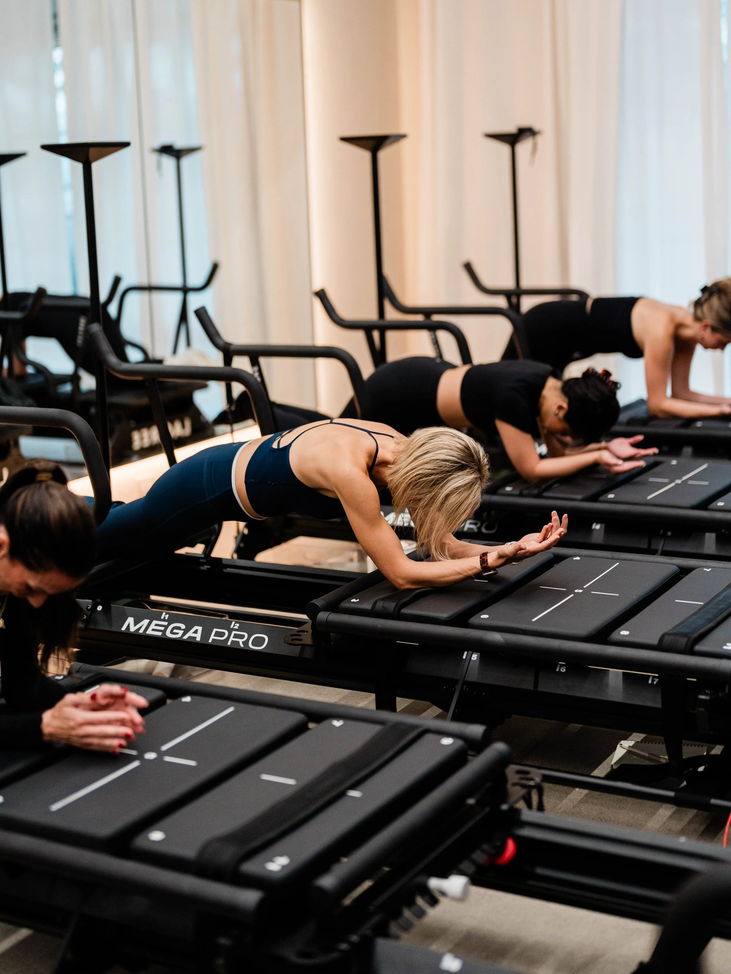 Women practicing Lagree on reformer machines in a fitness studio.