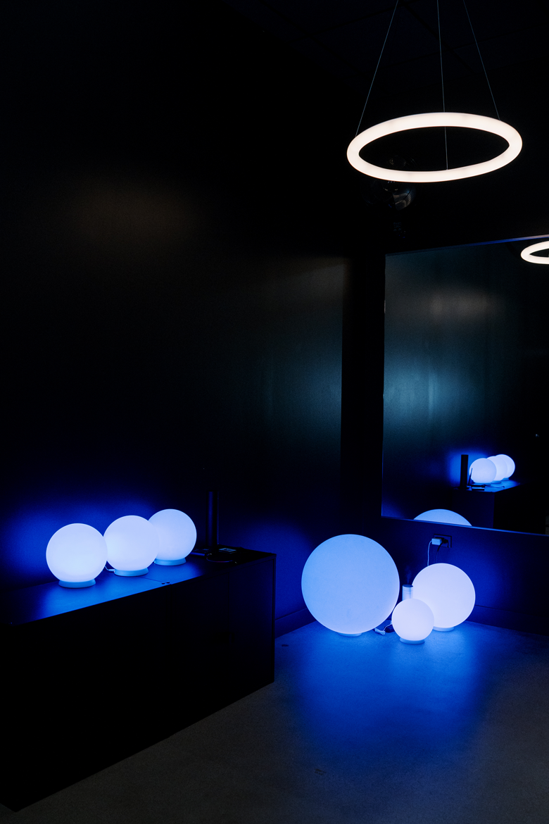 A dark room with glowing blue and white spherical lamps on and near a black cabinet, and modern pendant lighting fixtures hanging from the ceiling.