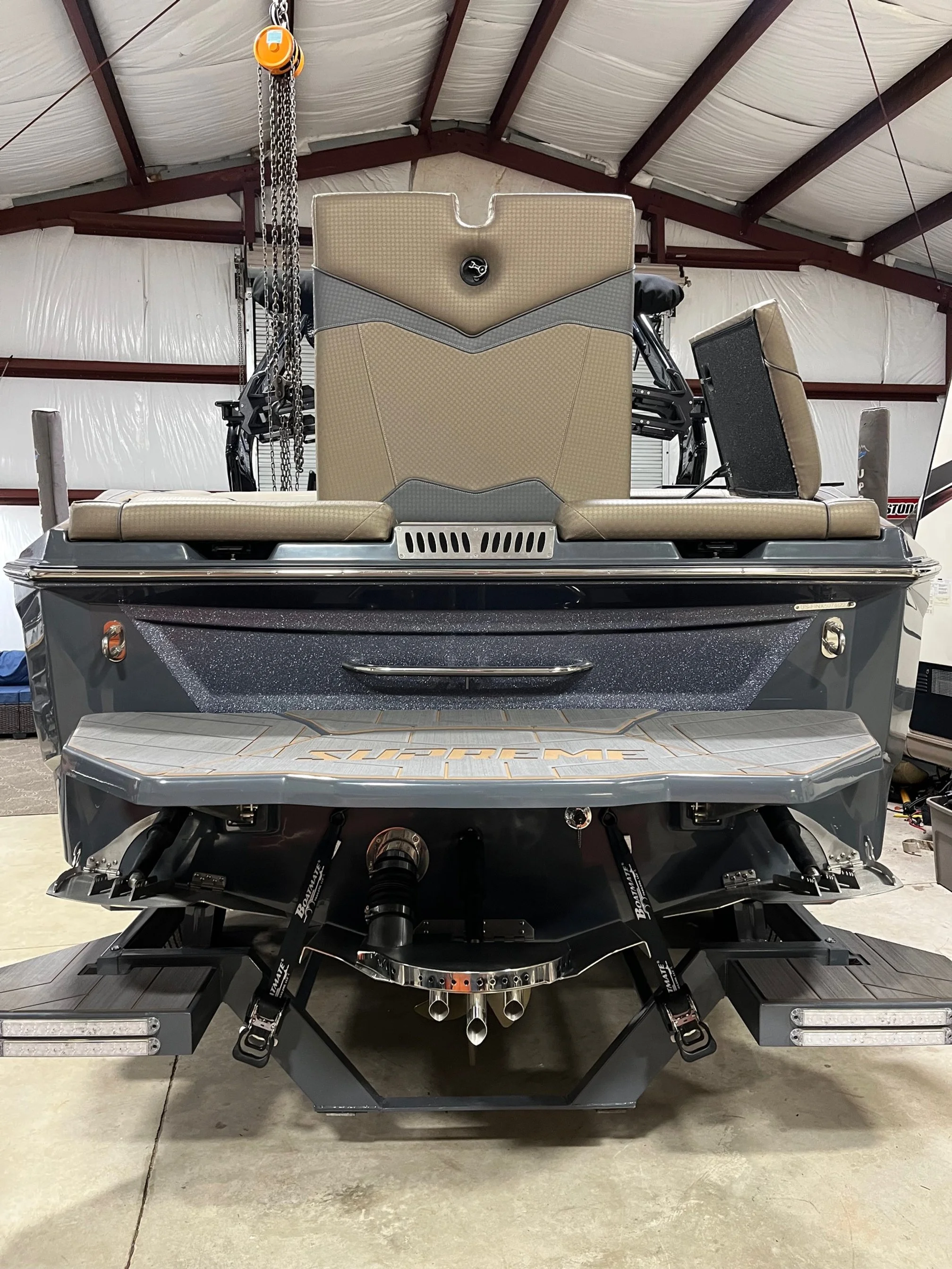 Front view of a high-performance speedboat boat engine wakeboarding in a warehouse, showing the engine compartment with dual exhaust pipes and suspension components.