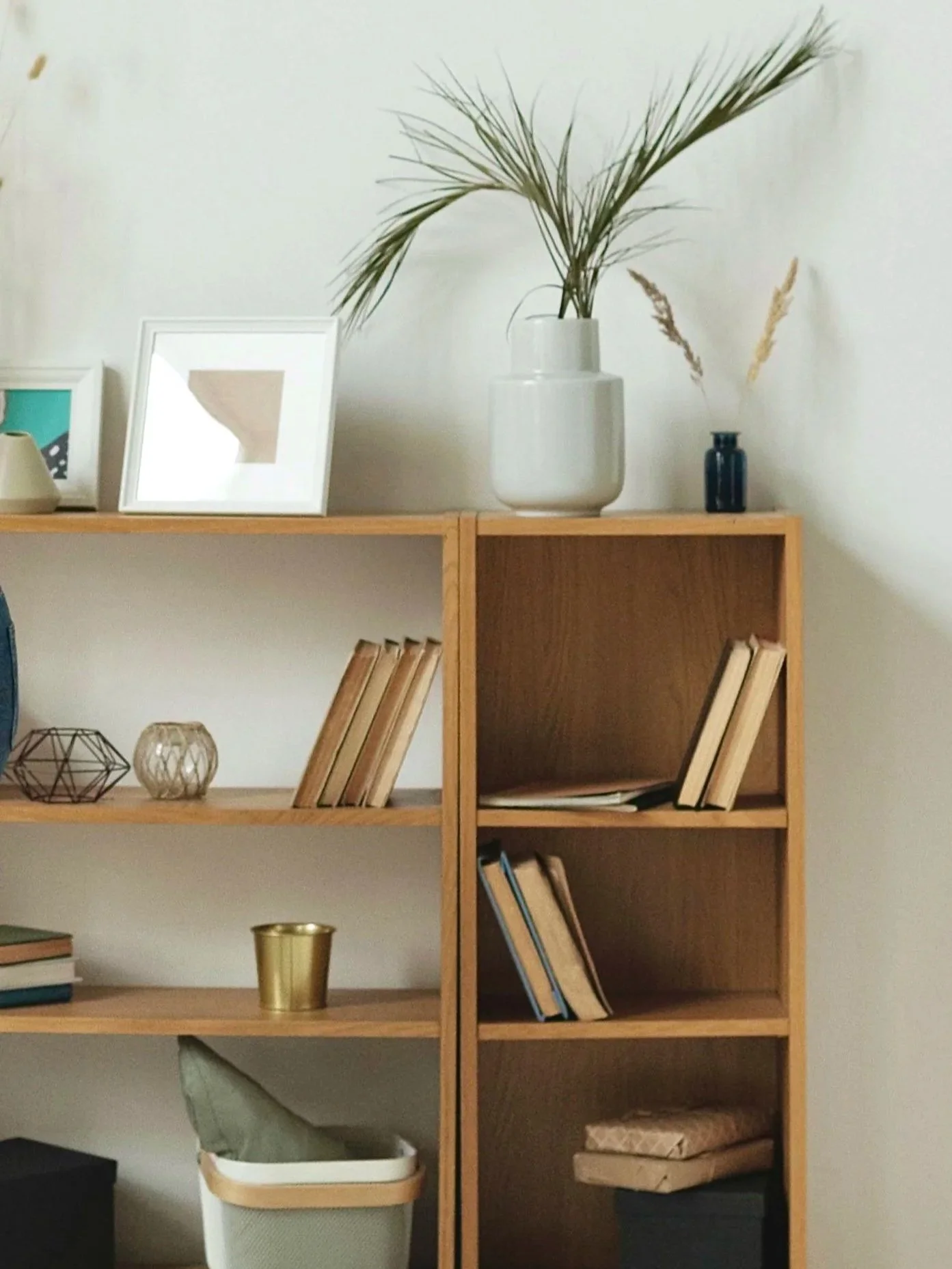 Wooden bookshelf with decorative items, books, and storage baskets, with a white wall background.