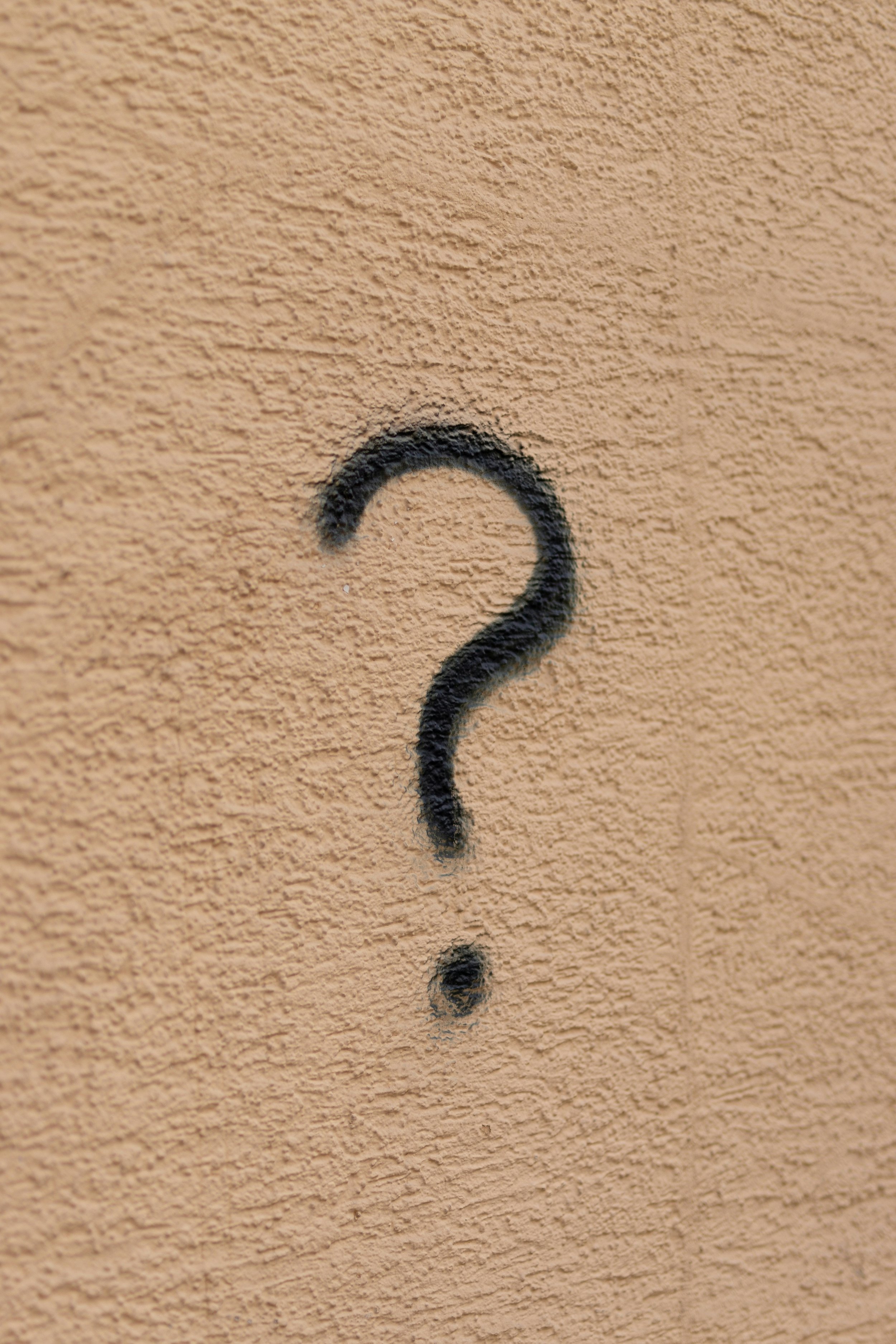 A beige wall with a black spray-painted question mark.